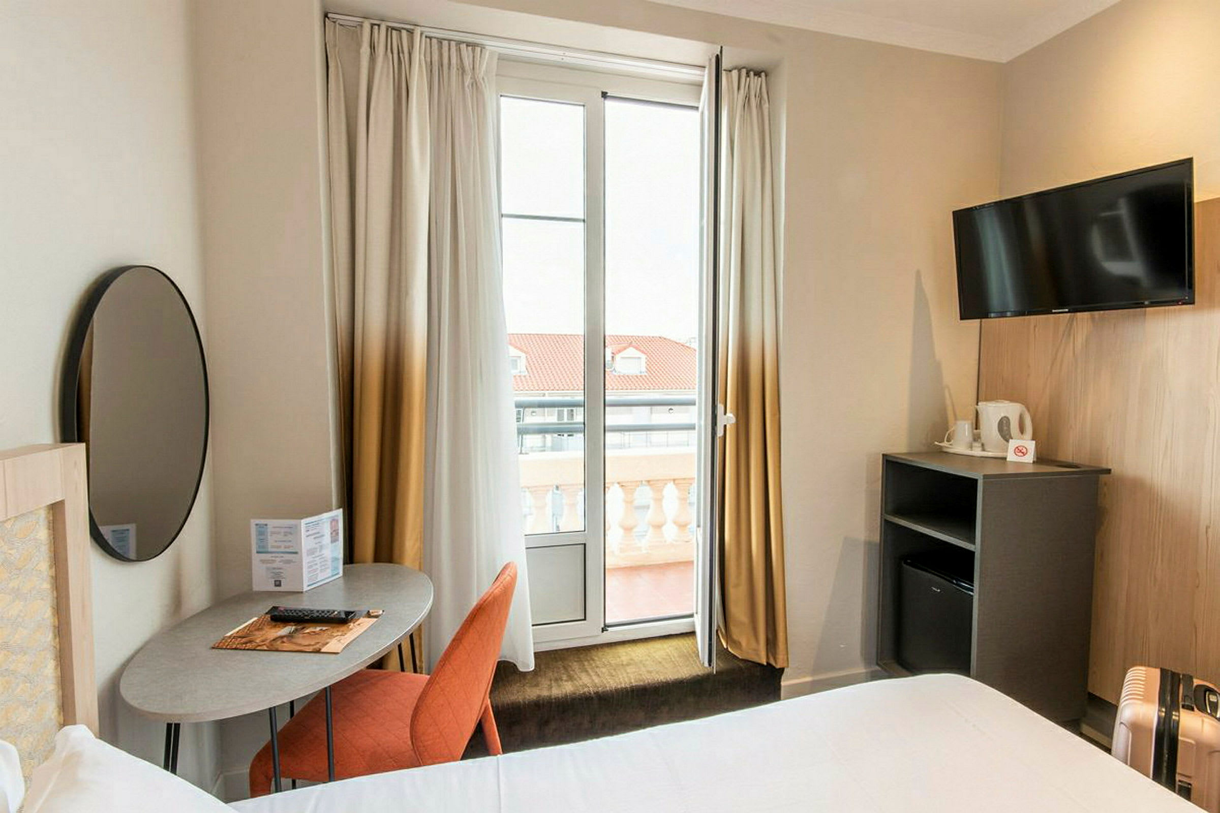Ett hotellrum med modern inredning, inklusive ett skrivbord, en stol, en TV och en balkong. (AI-genererad text)