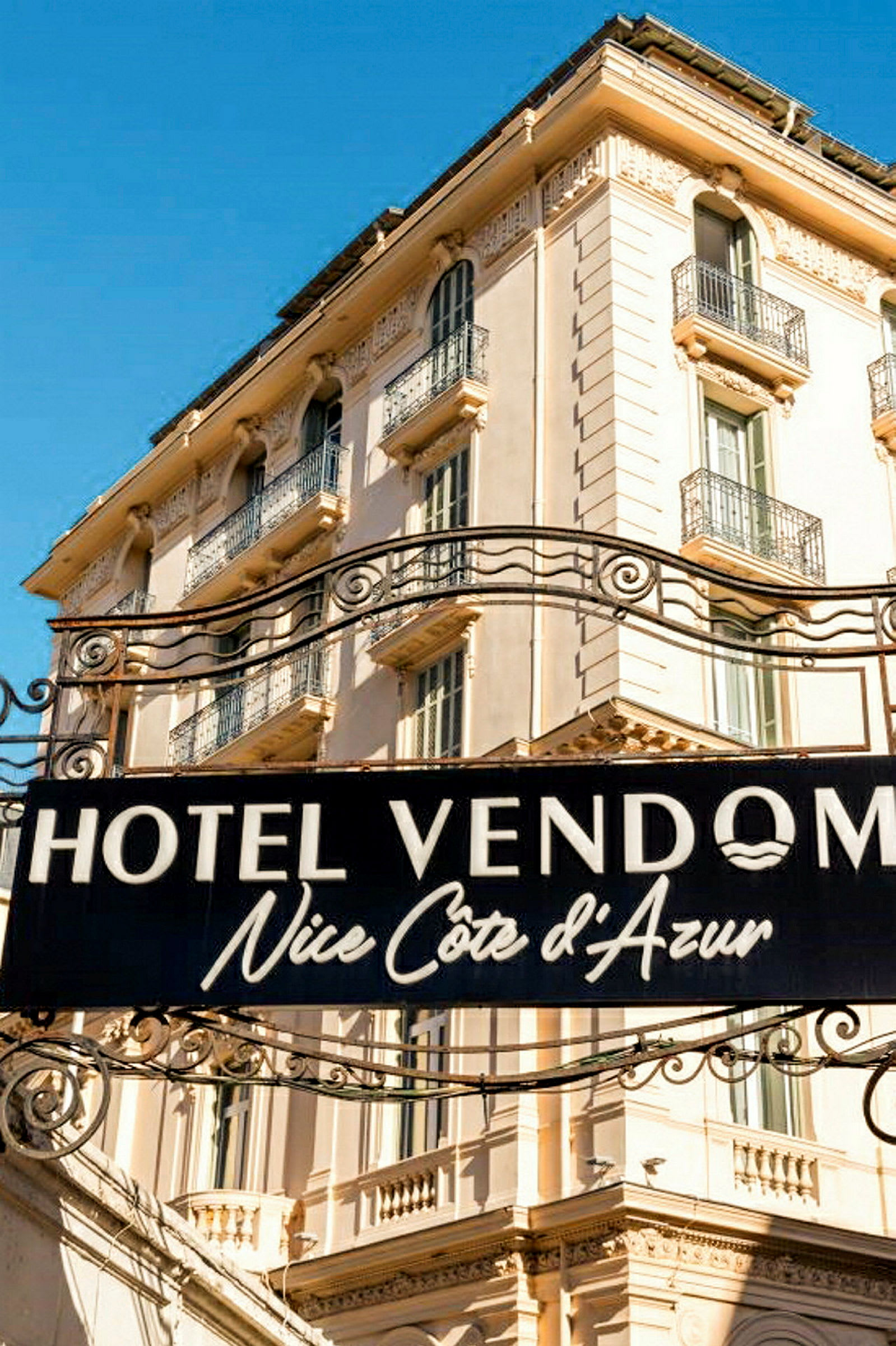 Skylt med texten Hotel Vendome Nice Côte d’Azur framför en beige byggnad. (AI-genererad text)