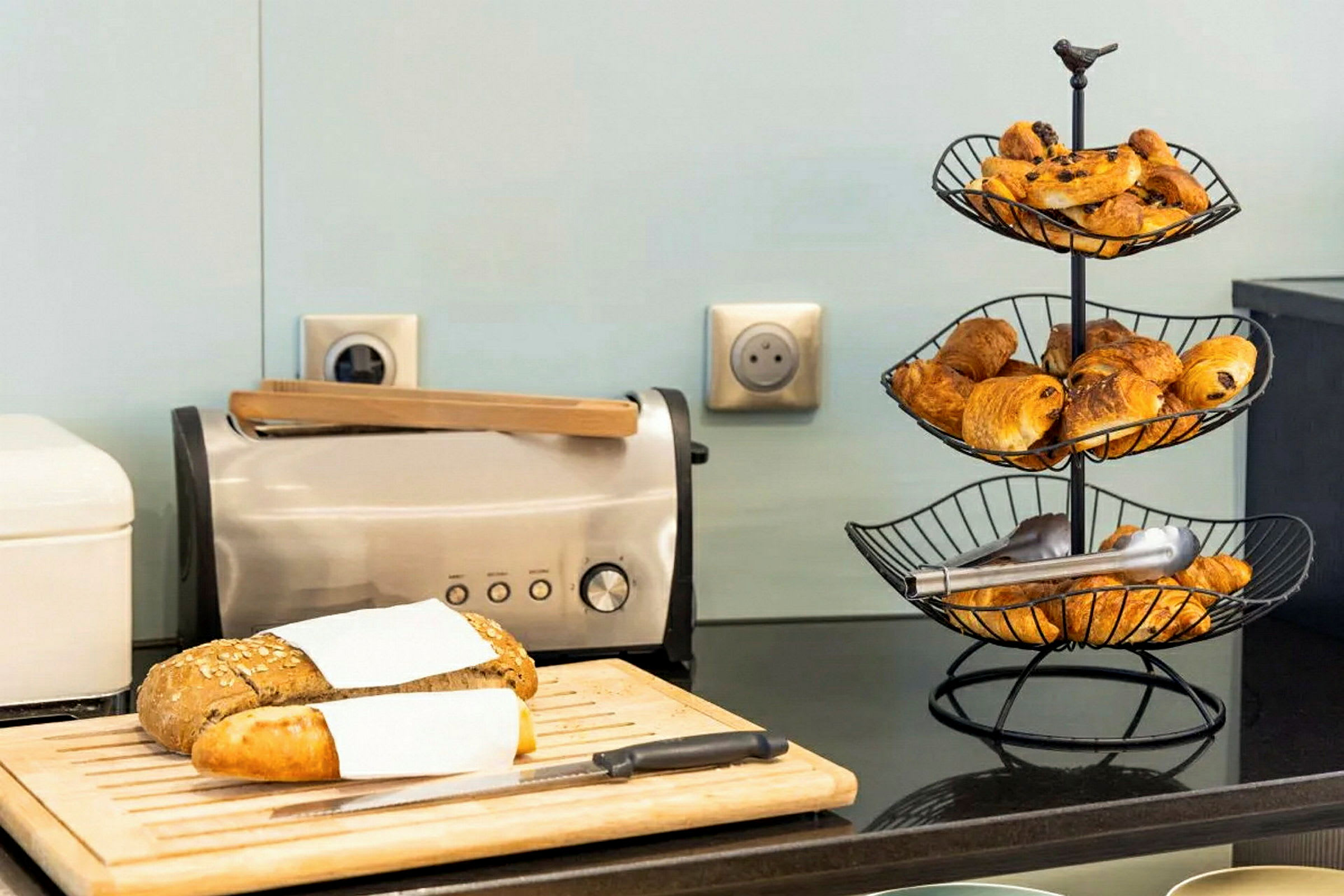 Bild på en brödskiva med en brödrost och ett brödväntställ med croissanter på en köksbänk. (AI-genererad text)