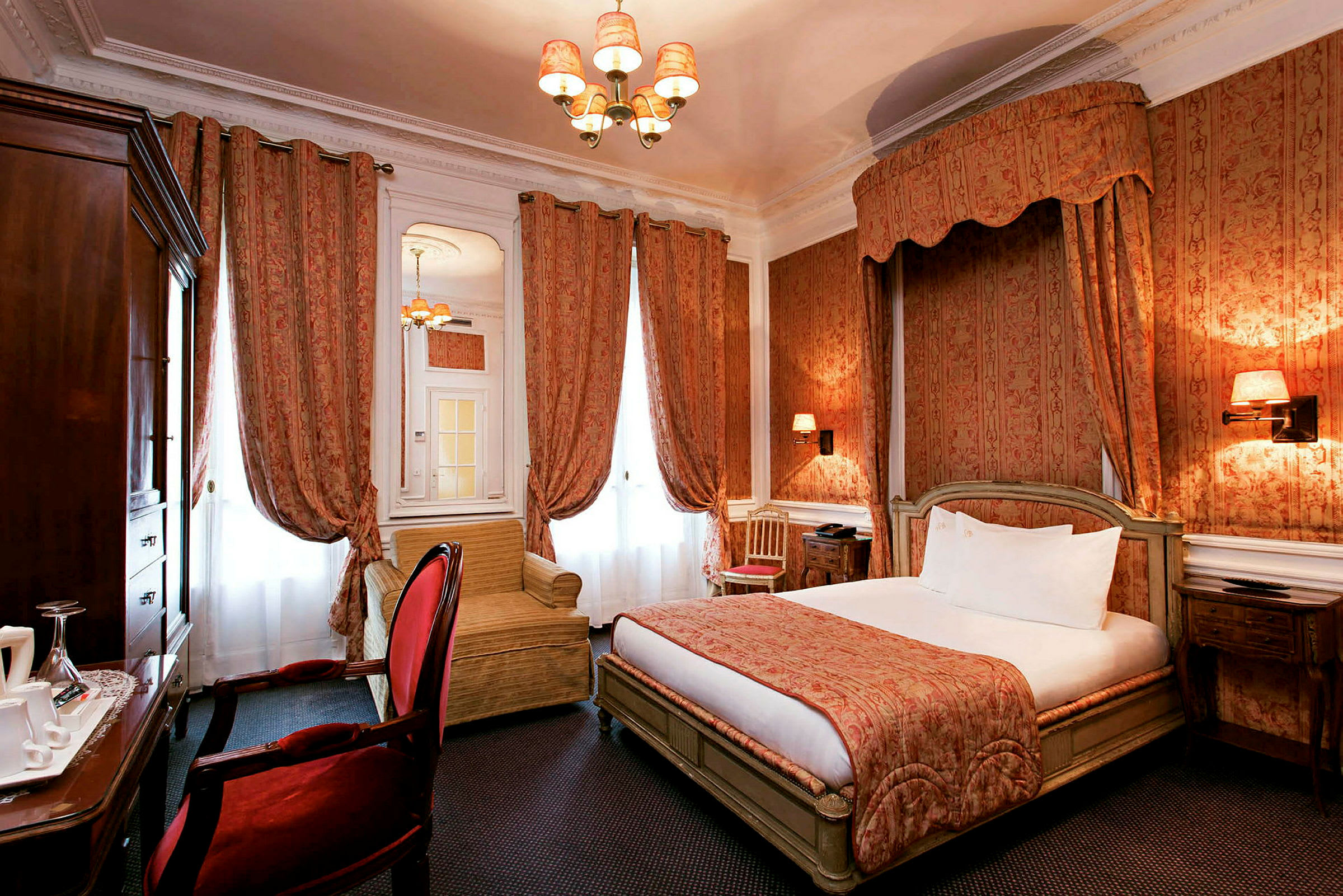 Ett hotellrum med en inredning i klassisk stil, med en dubbelsäng, röda gardiner och en fåtölj. (AI-genererad text)