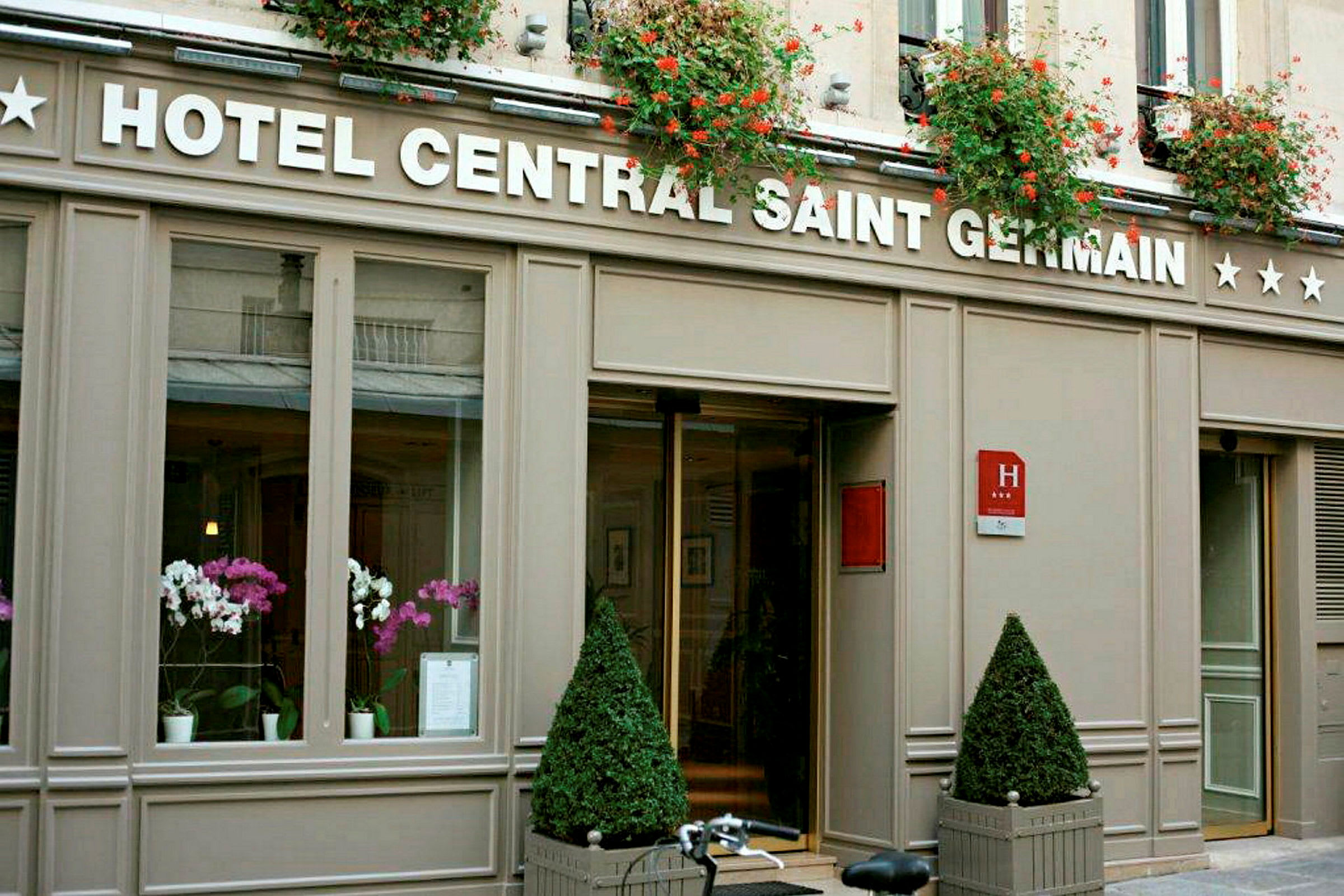 Bild av hotellentrén till Hotel Central Saint Germain med blomdekorationer och skylten synlig. (AI-genererad text)