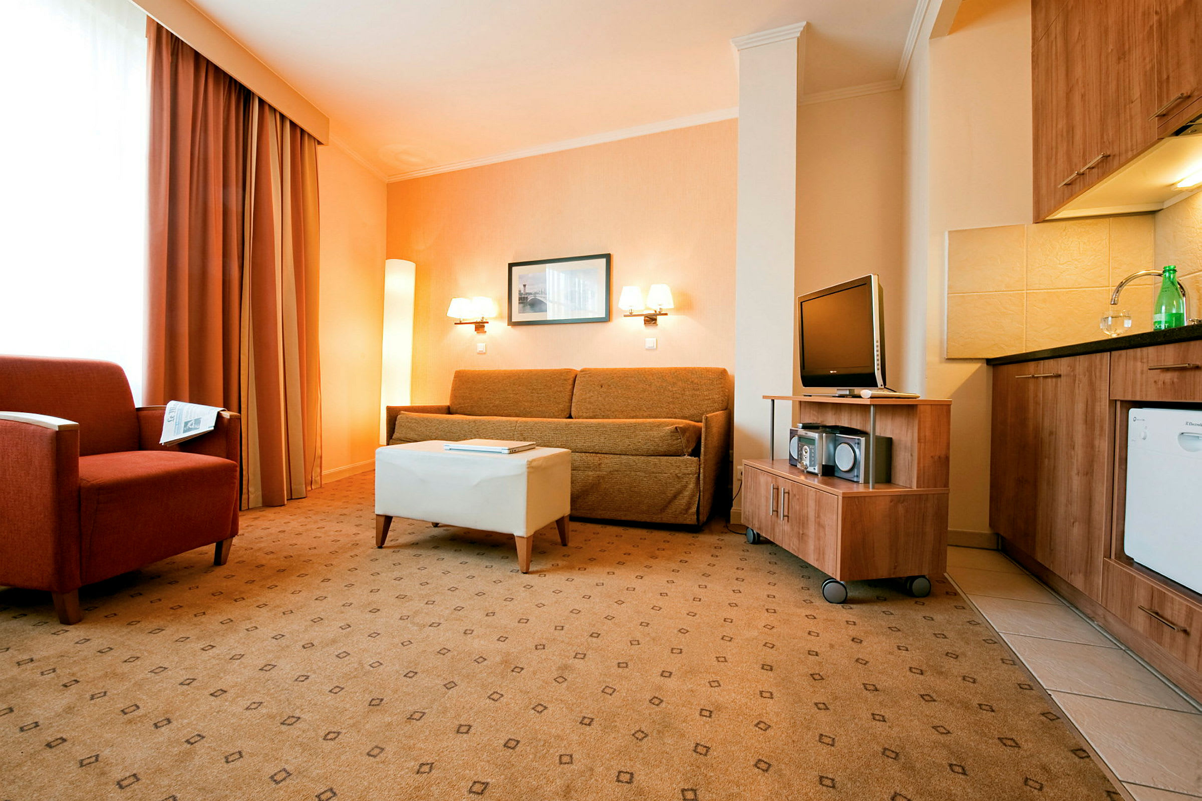 Ett hotellrum med en soffa, fåtölj och TV tillsammans med ett kök. (AI-genererad text)