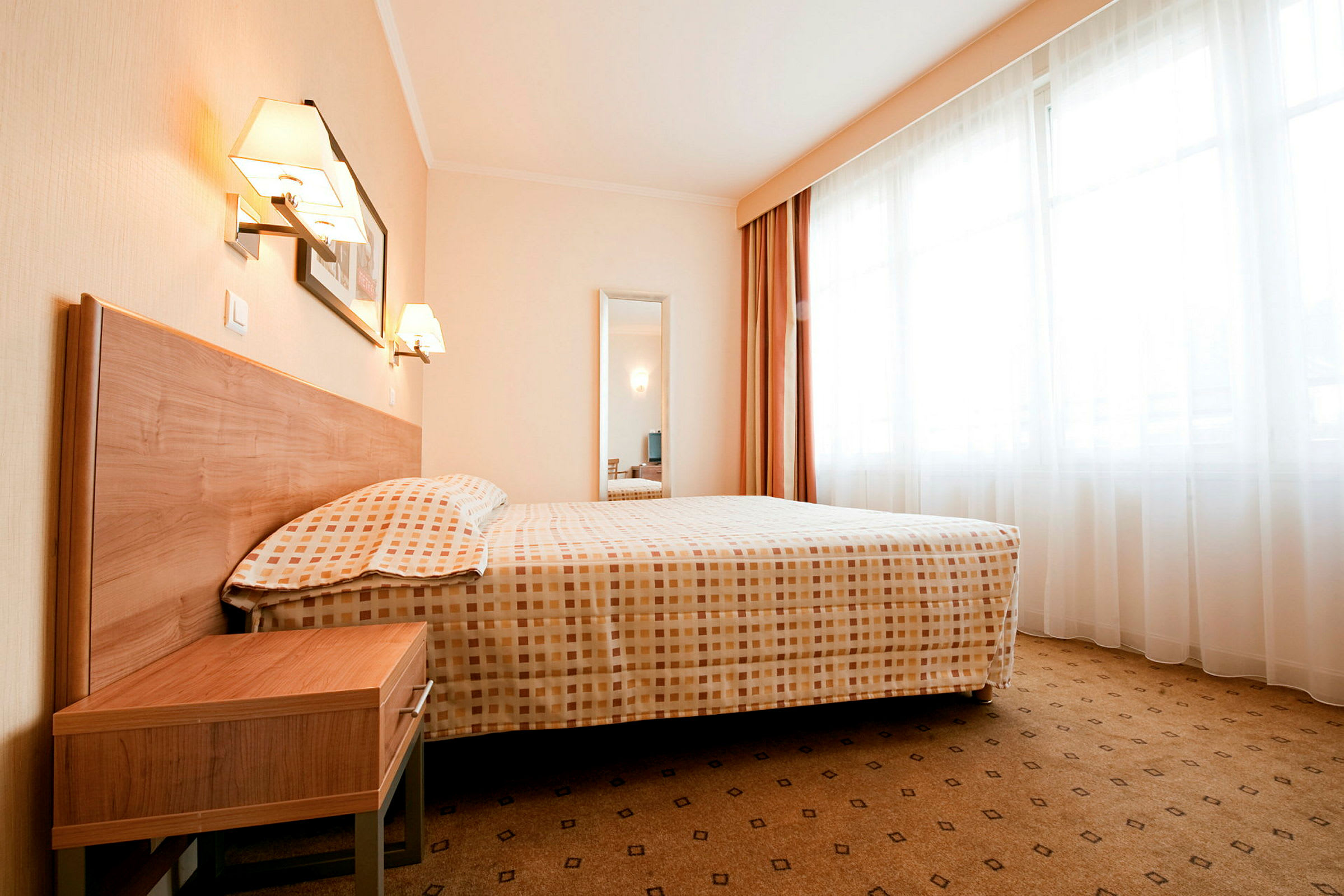 Ett hotellrum med en stor säng, nattduksbord och fönster med gardiner. (AI-genererad text)
