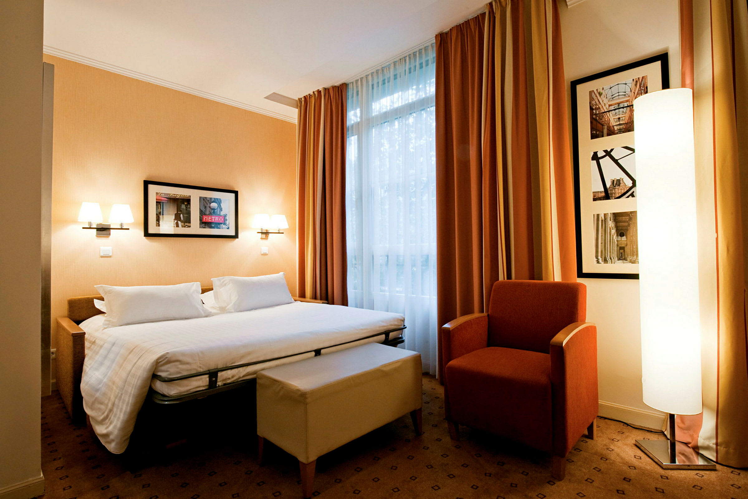 Ett hotellrum med en säng, en fåtölj och ett fönster med gardiner. (AI-genererad text)