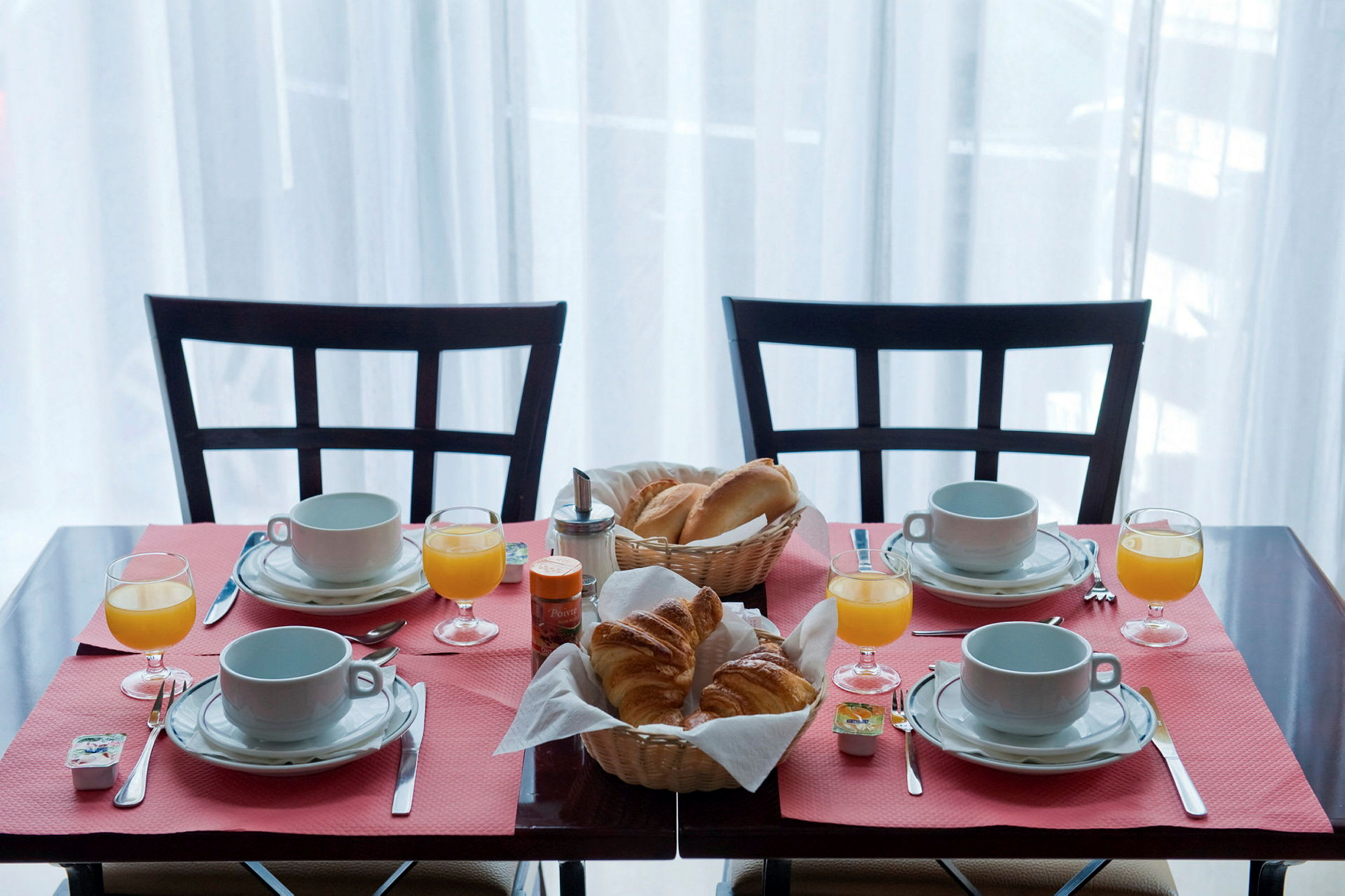 Ett frukostbord dukat för fyra personer med kaffekoppar, glas med apelsinjuice och korgar med bröd och croissanter. (AI-genererad text)