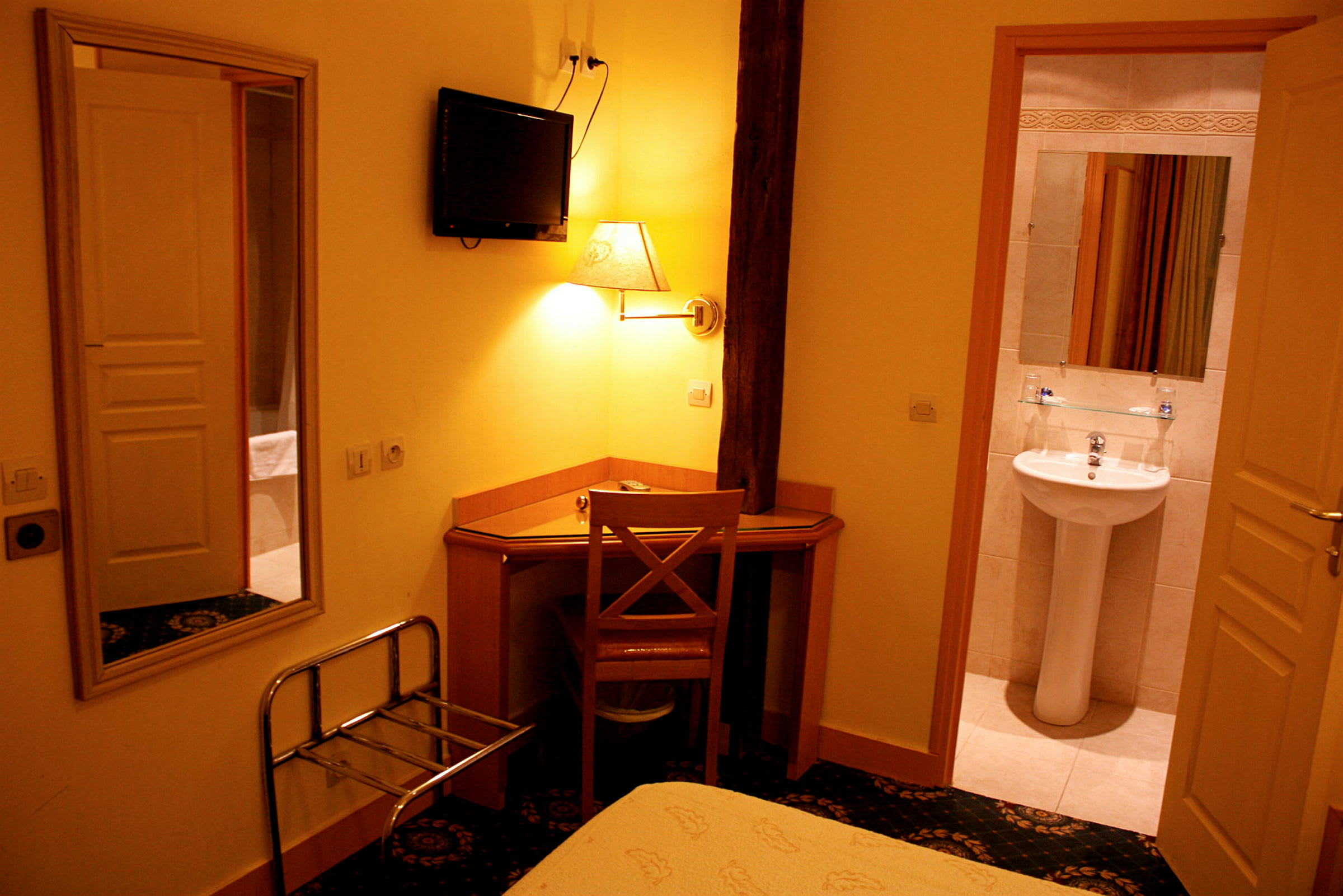 Hotellrum med skrivbord och stol, väggmonterad TV samt öppnad dörr till badrum med ett handfat. (AI-genererad text)