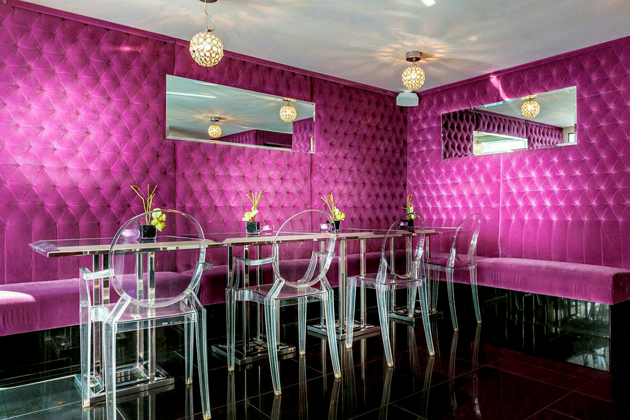 En modern och färgstark restaurang eller lounge med fuchsiafärgad vadderad väggpanel, genomskinliga stolar och spegeldekorationer. (AI-genererad text)