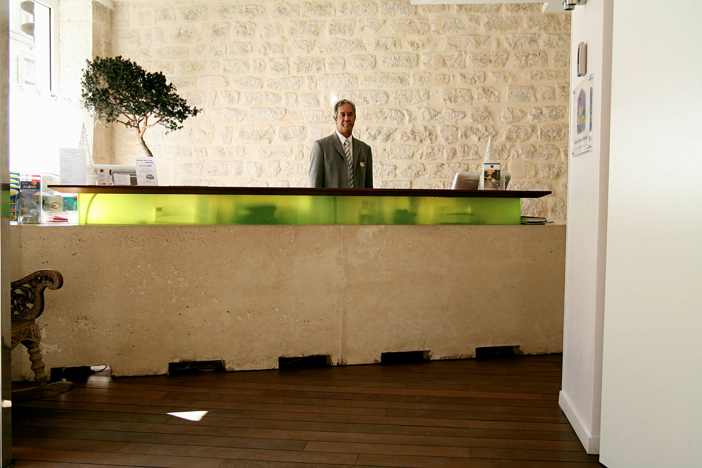 Bild på en hotellreception med en modern disk i betong och glas, samt en stenklädd vägg i bakgrunden. (AI-genererad text)