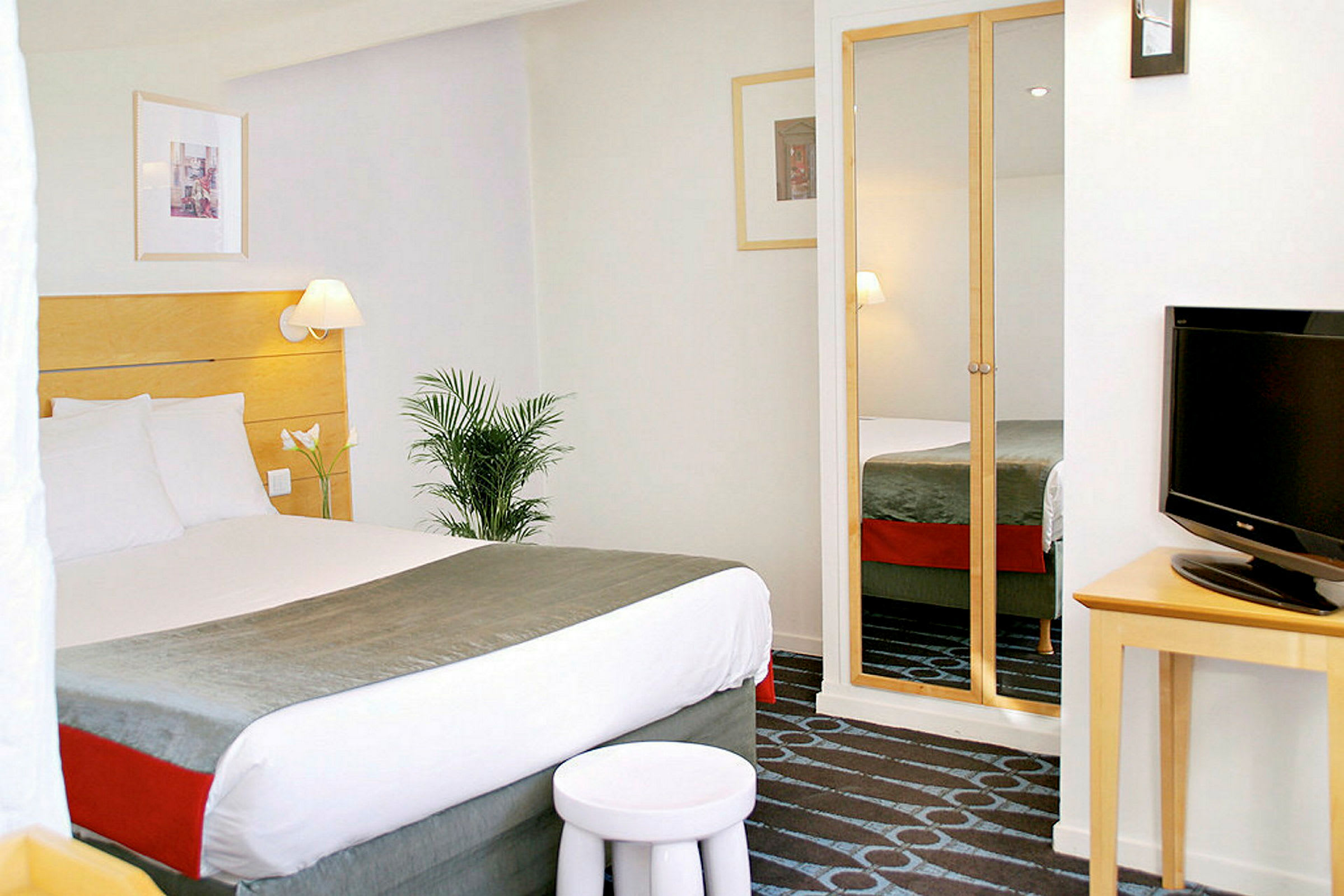 Hotellrum med en bäddad dubbelsäng, TV och spegelklädd garderob. (AI-genererad text)