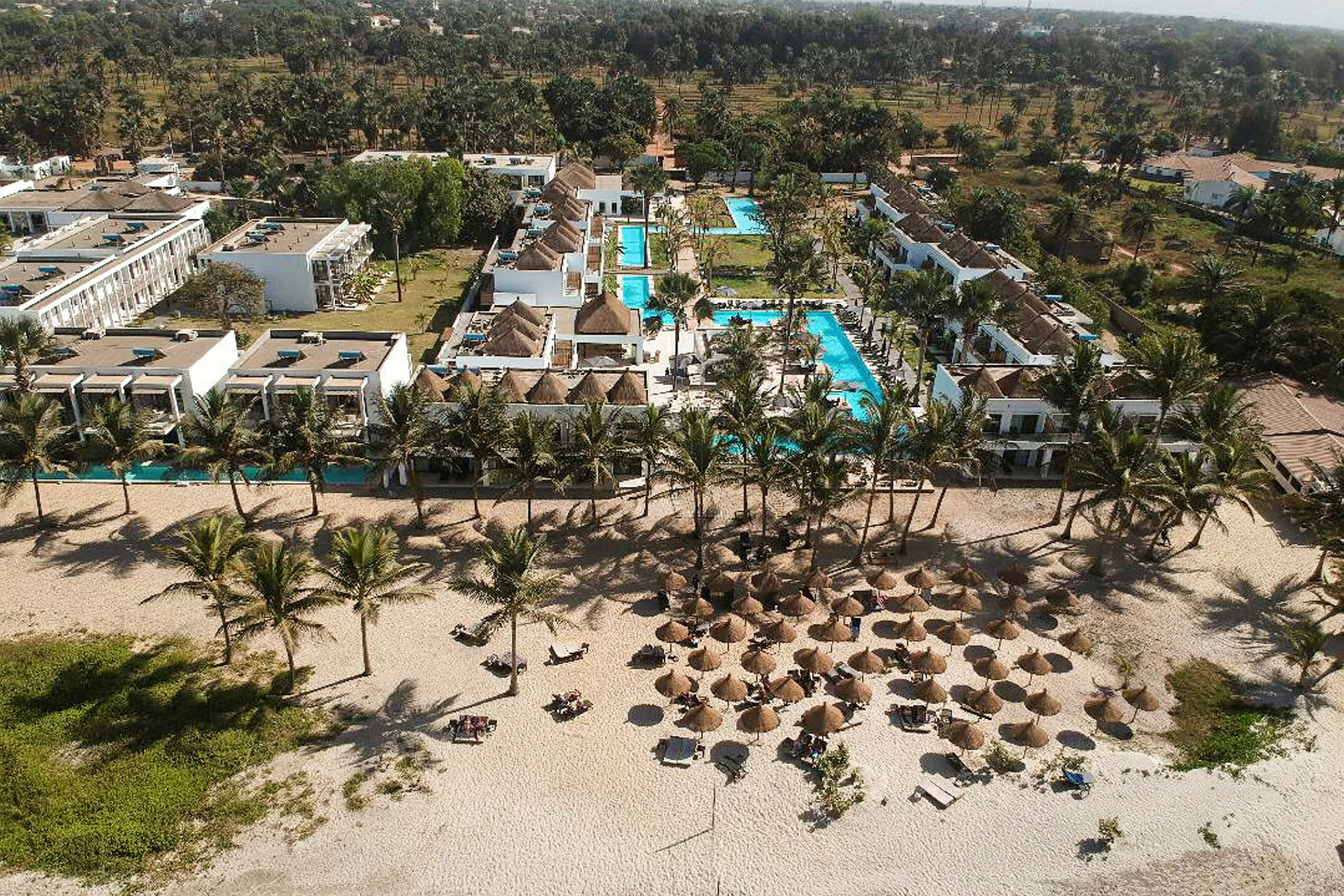 Flygfotografi av en resort med pooler, tropiska palmer och strand med parasoller. (AI-genererad text)