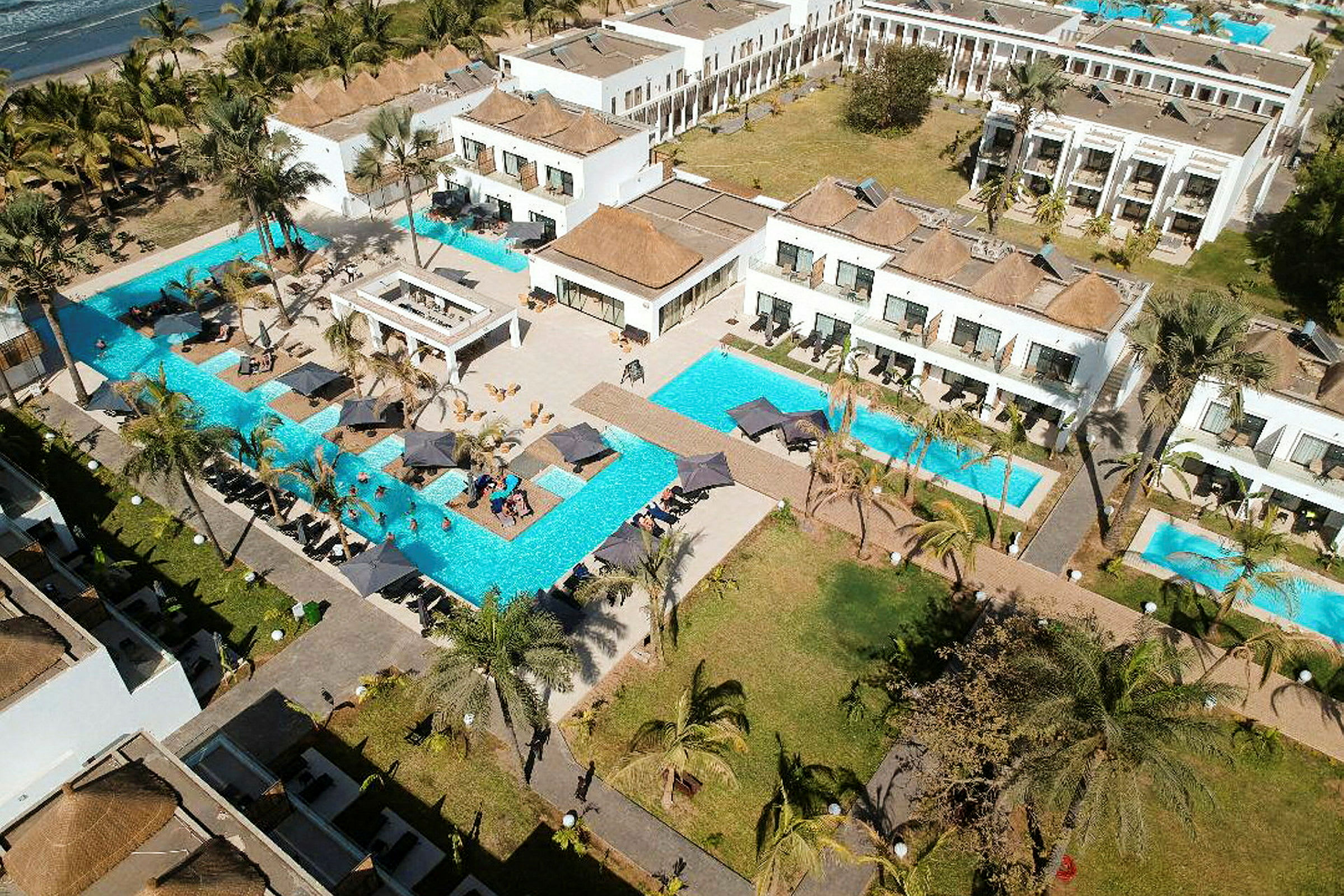 Bild av en resort med flera vita byggnader, omgivna av pooler och palmer. (AI-genererad text)