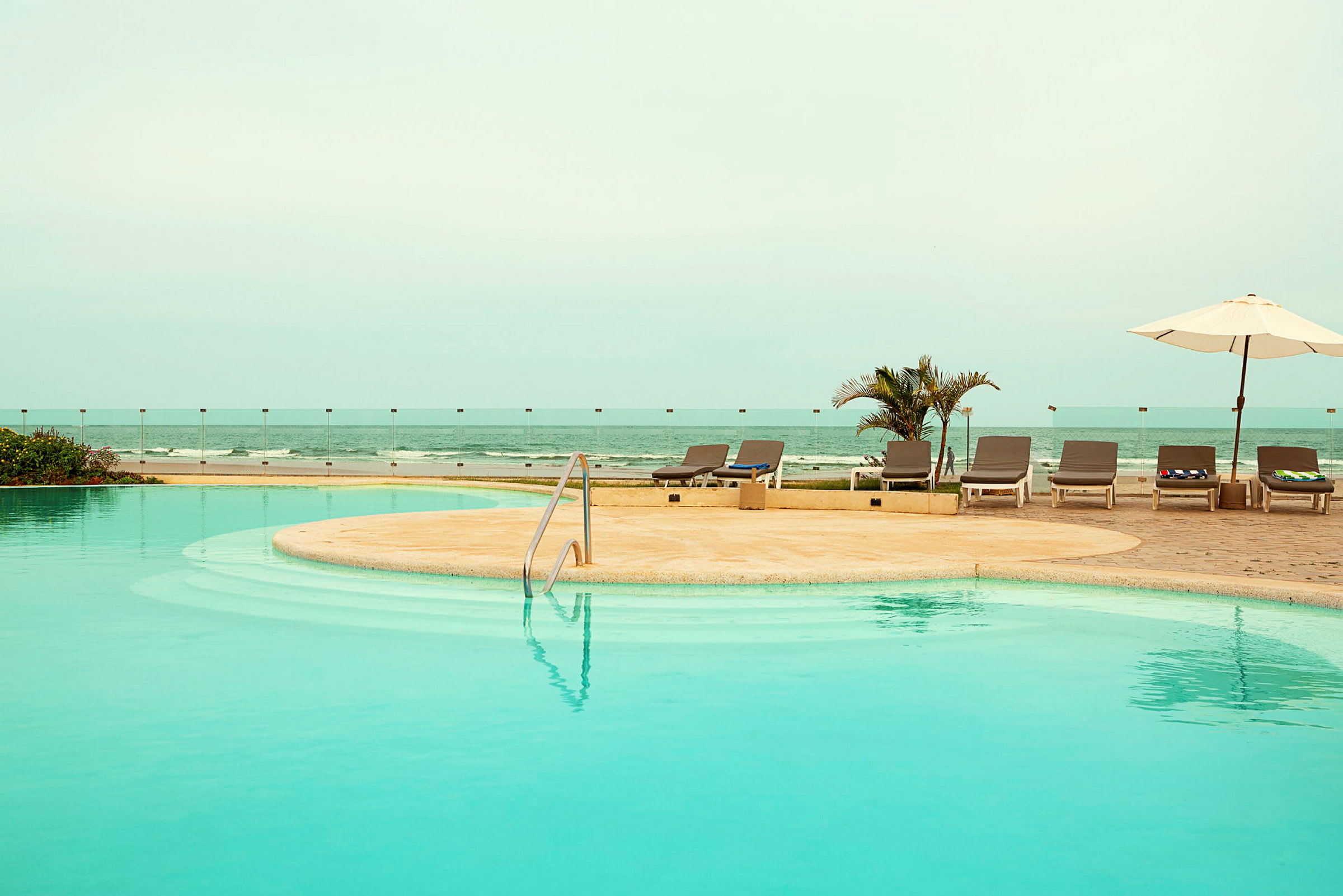 En pool med solstolar och parasoll vid havet. (AI-genererad text)