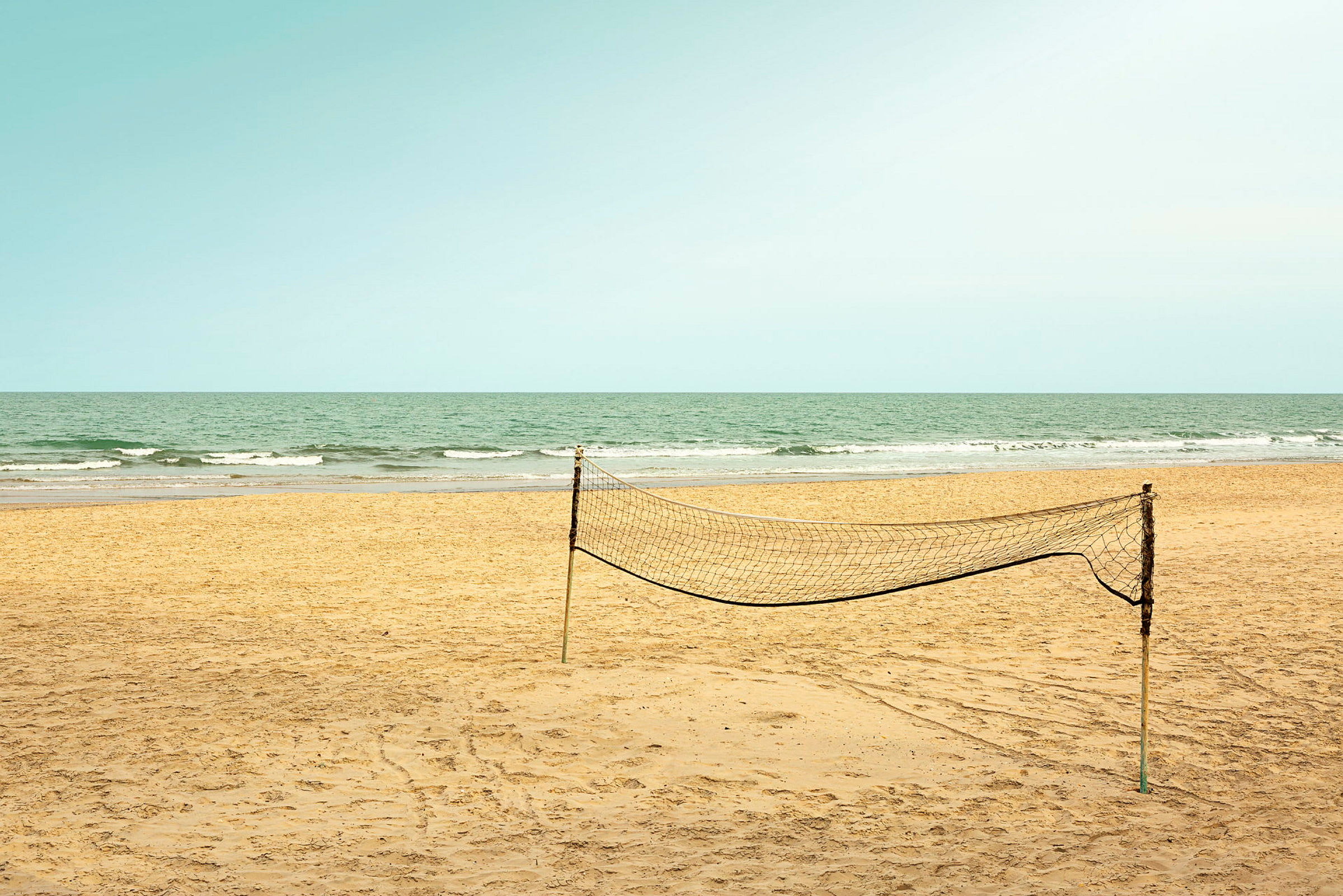 En tom sandstrand med ett uppsatt volleybollnät och havet i bakgrunden. (AI-genererad text)