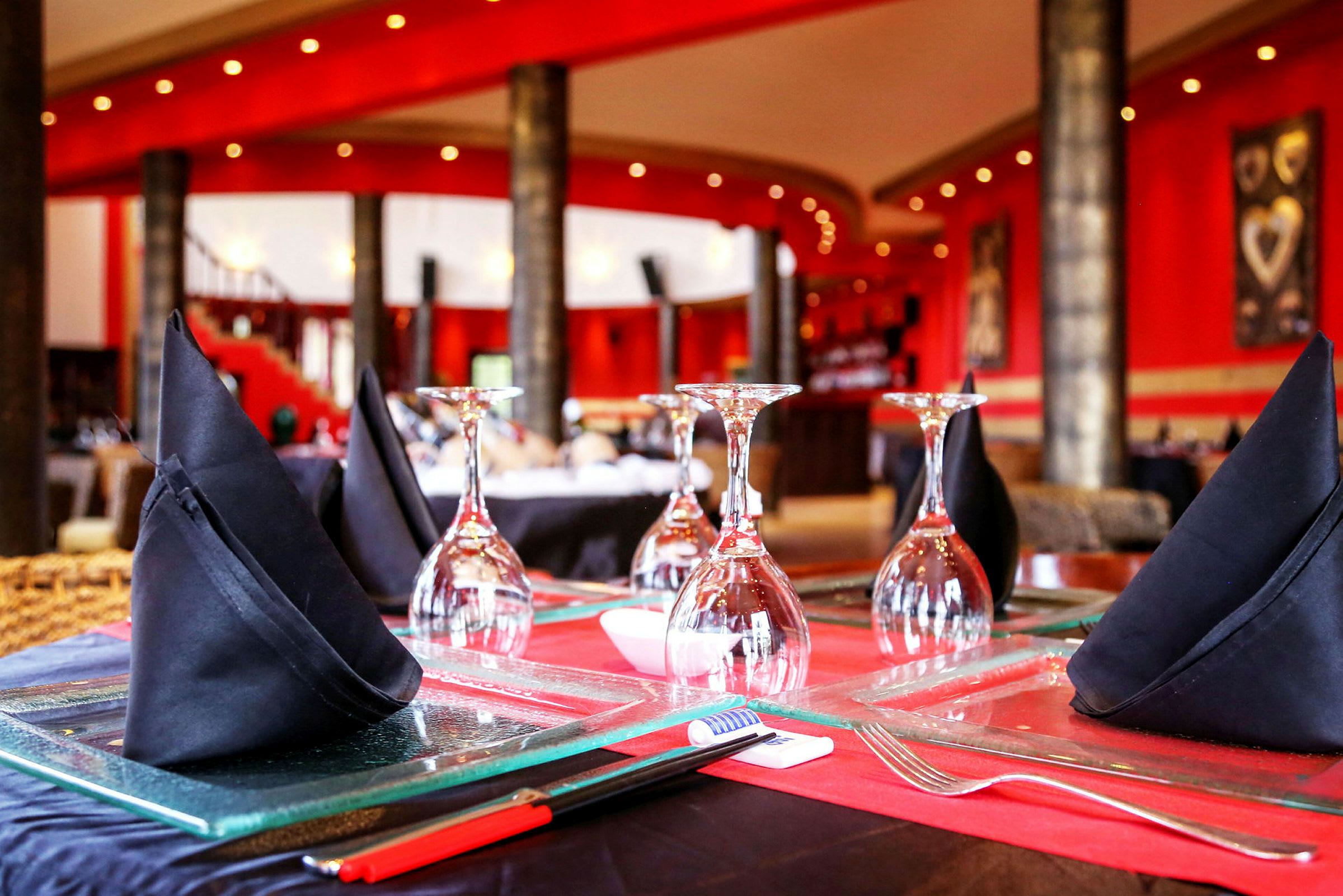 Närbild på en restauranguppdukning med glas och svarta tygservetter på ett bord, omgivningen är elegant med röda väggar. (AI-genererad text)