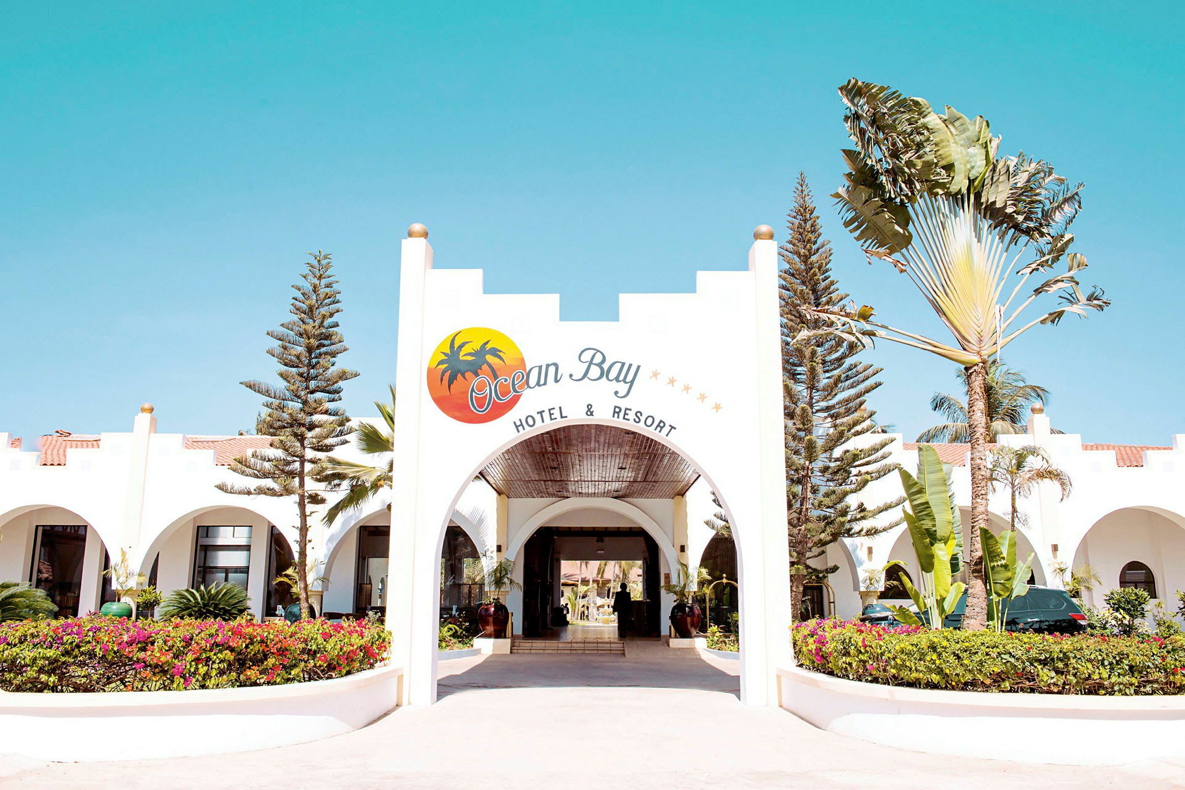 Ingången till Ocean Bay Hotel & Resort, med en välvd öppning och omgivande grönska. (AI-genererad text)