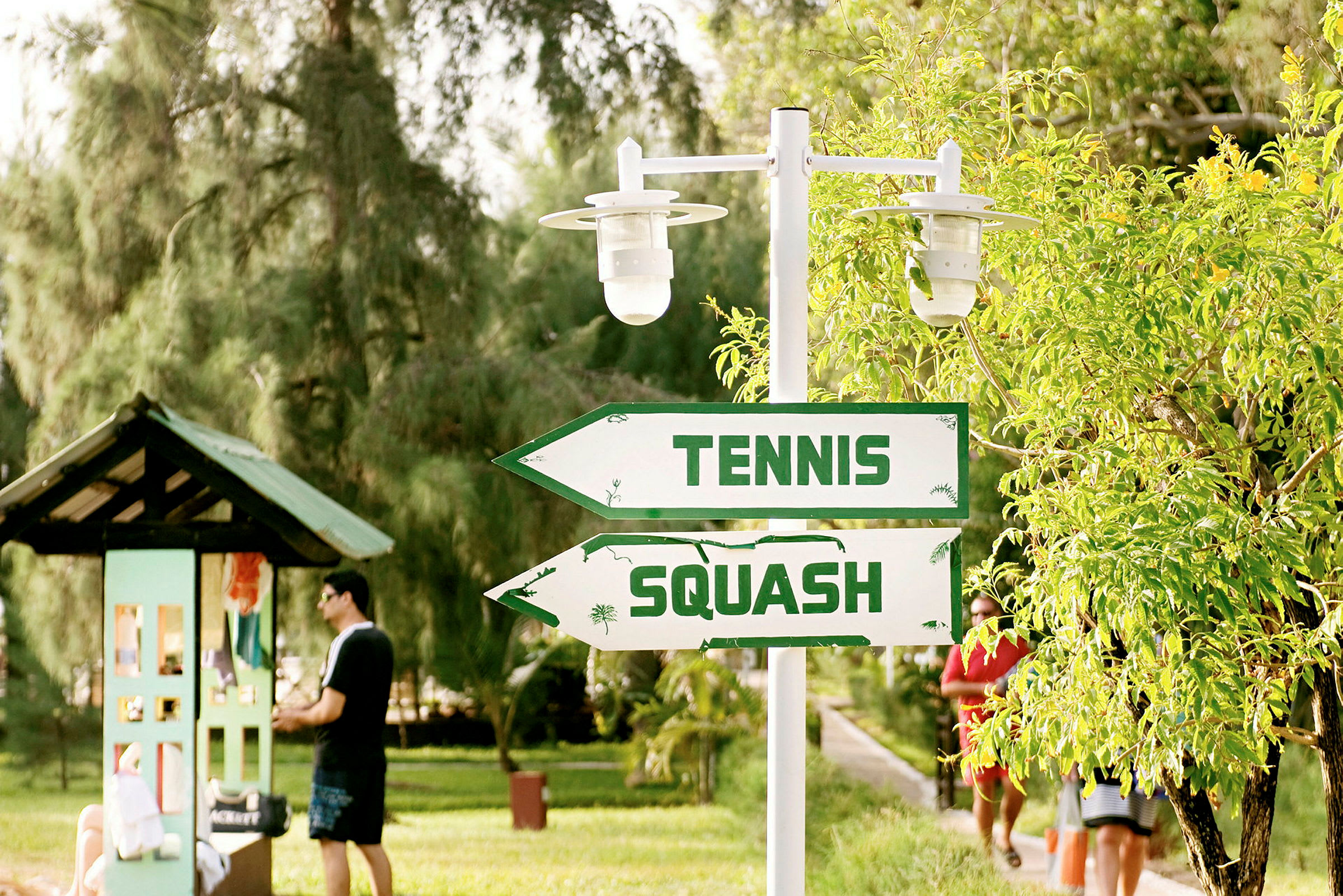 Skyltar med texten 'Tennis' och 'Squash' i en grönskande miljö. (AI-genererad text)
