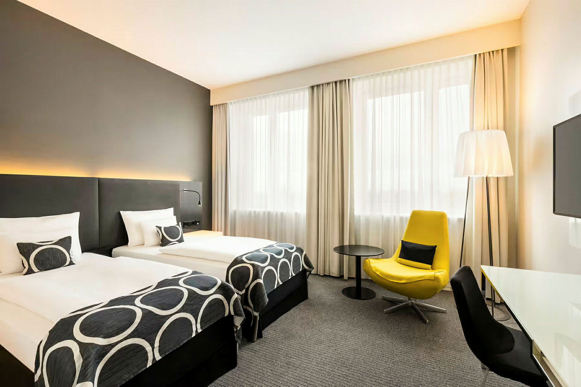 Ett hotellrum med två enkelsängar, en gul fåtölj och ett skrivbord. (AI-genererad text)