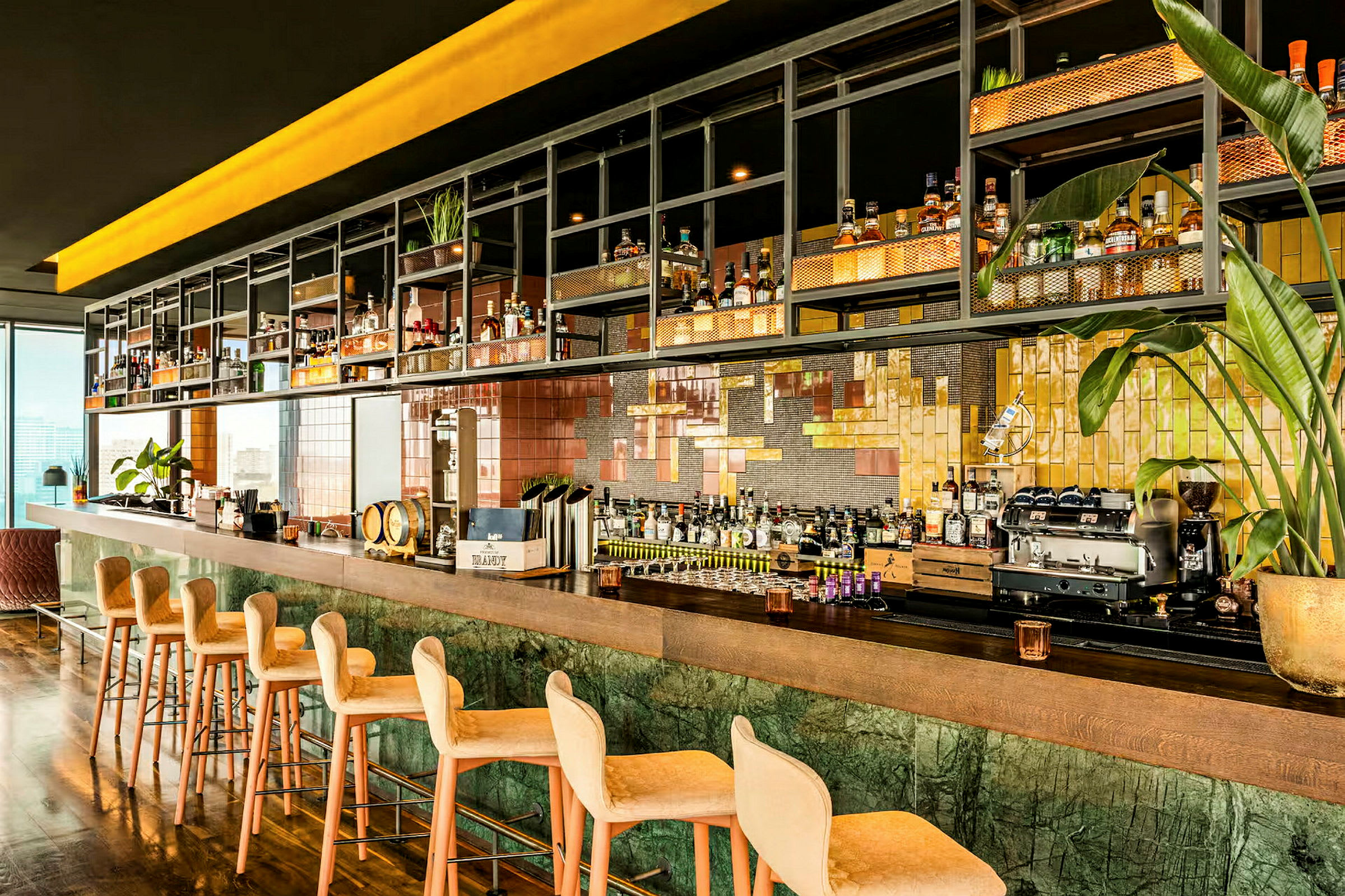 En modern bar med höga stolar framför en lång bardisk, omgiven av hyllor fyllda med flaskor och dekorationer. (AI-genererad text)