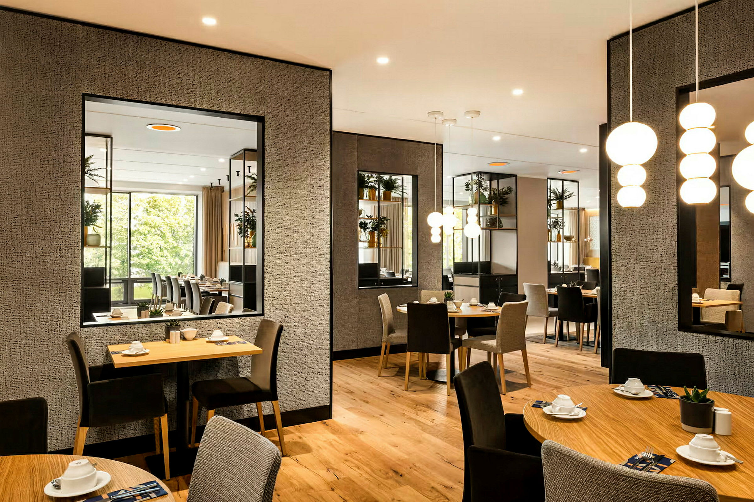 Ett välbelyst kafé eller restaurang med moderna bord och stolar, prydnadsväxter samt speglar på väggarna. (AI-genererad text)