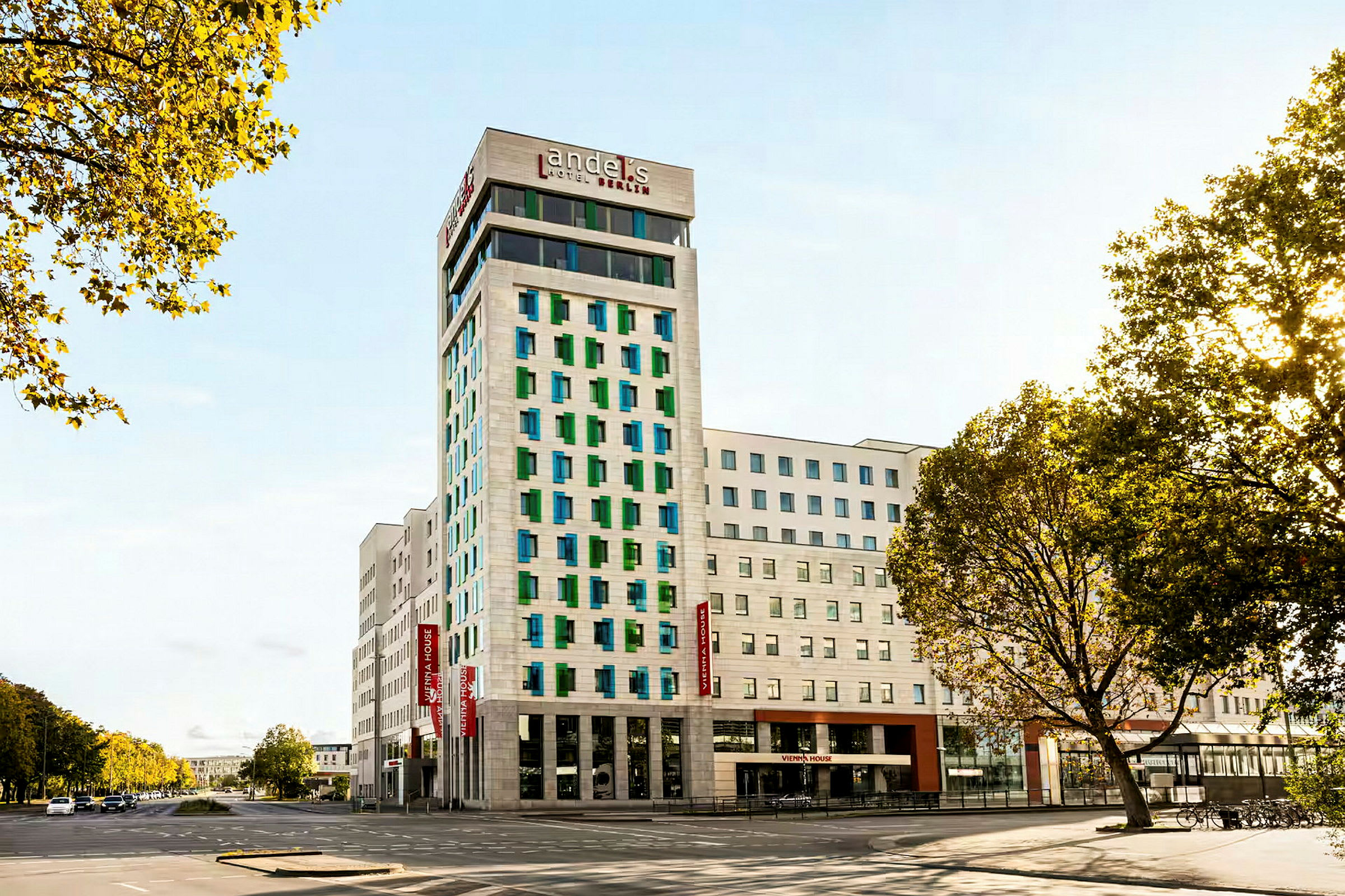En modern hotellbyggnad med vit fasad och färgade fönster, omgiven av vägar och träd. (AI-genererad text)