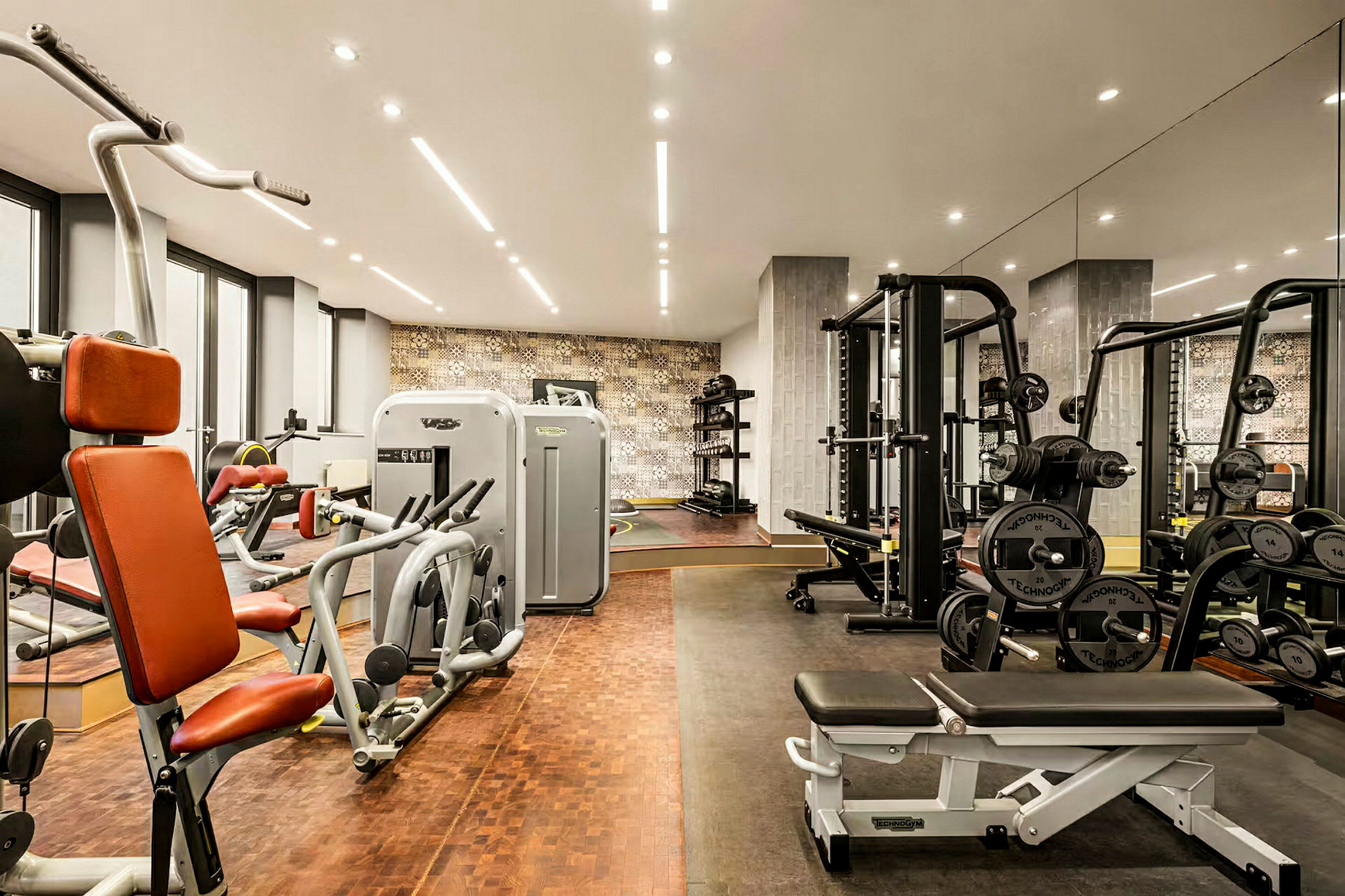 Ett gym utrustat med olika träningsmaskiner, fria vikter och bänkar, med spegelväggar och modern belysning. (AI-genererad text)