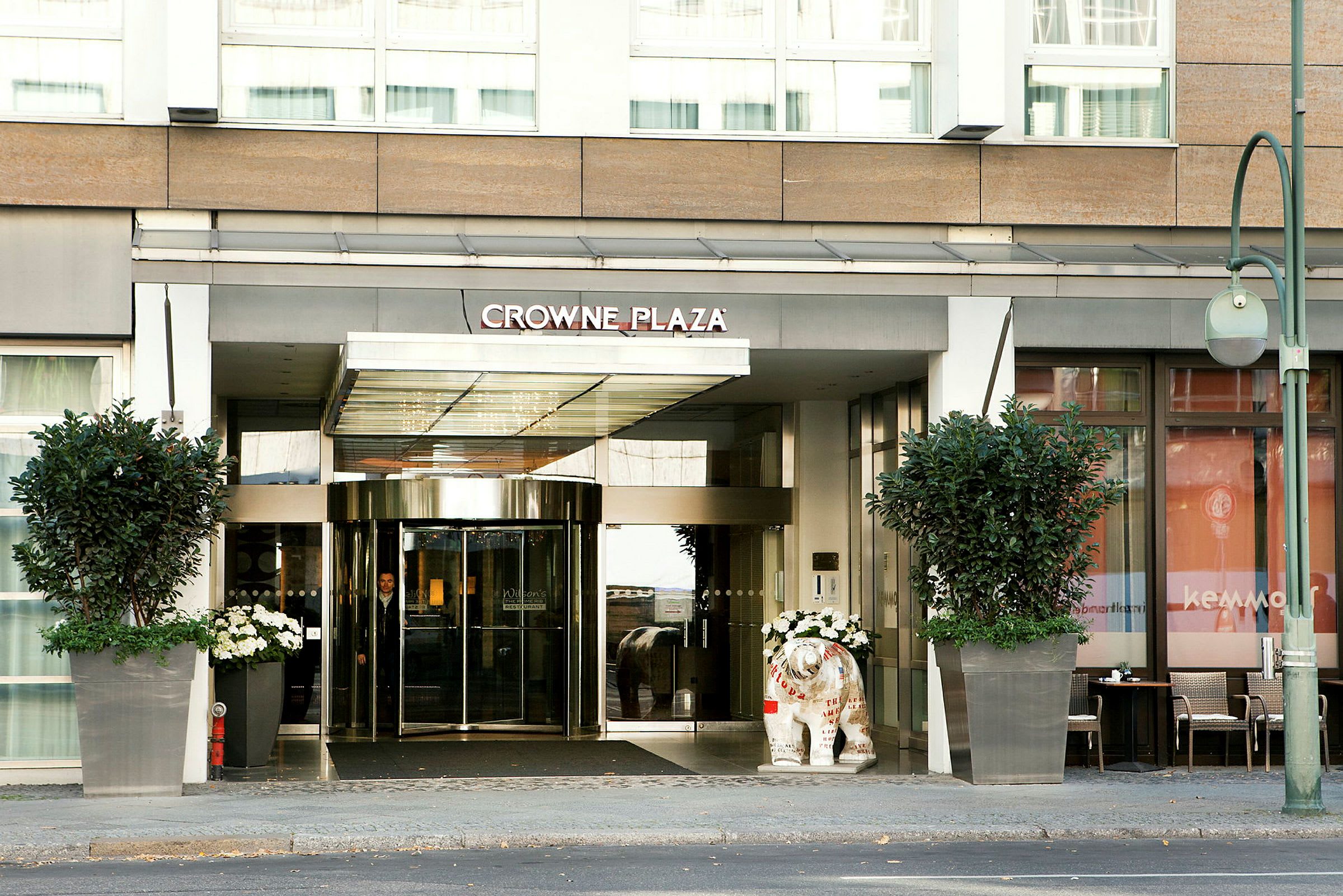 Ingången till hotell Crowne Plaza med glasdörrar och stora blomkrukor. (AI-genererad text)