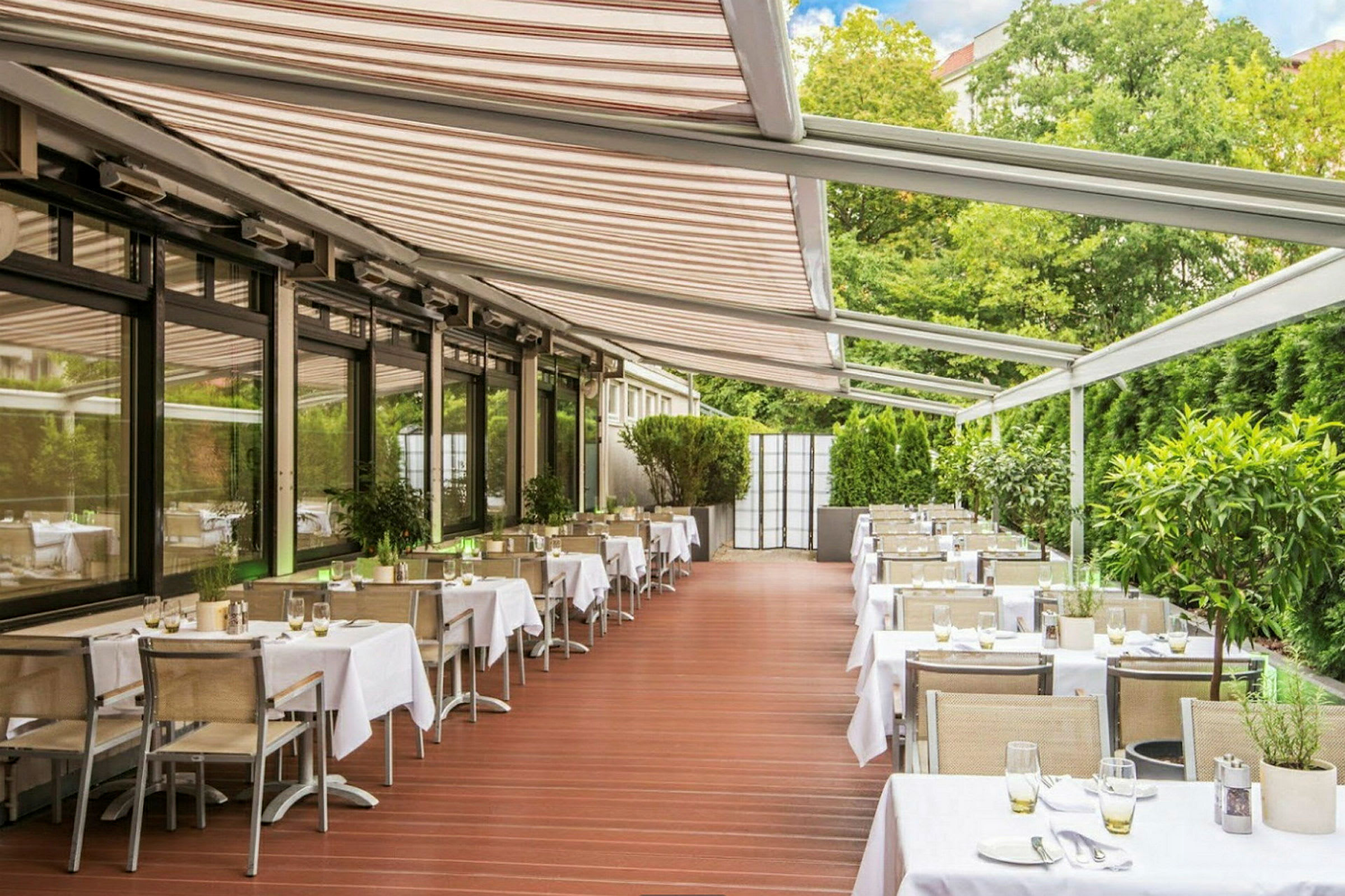 Bild av en restaurang med bord och stolar under en pergola med gröna växter runtomkring. (AI-genererad text)