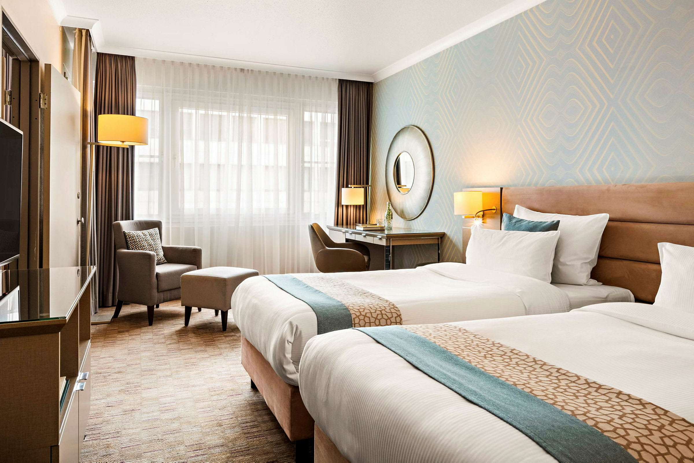 Ett hotellrum med två enkelsängar, skrivbord, stol och fåtölj. (AI-genererad text)