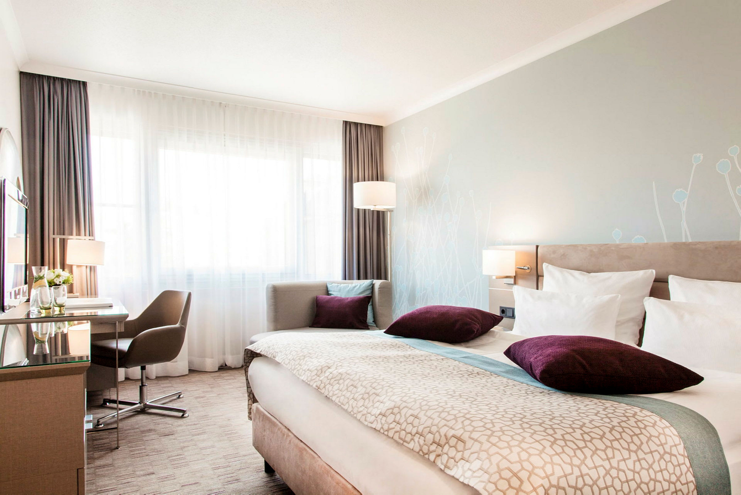 Ett hotellrum med en bred säng, en skrivbord och stol vid fönstret och mjuk belysning. (AI-genererad text)