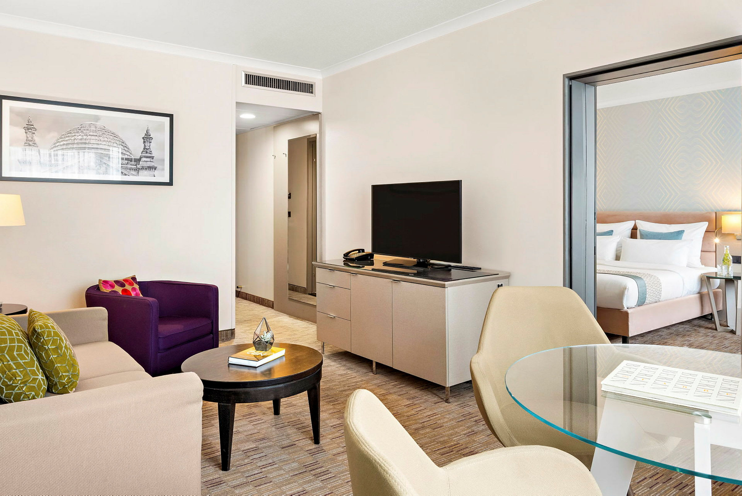 Vardagsrum i hotellsvit med sittmöbler, TV och öppning till sovrum. (AI-genererad text)