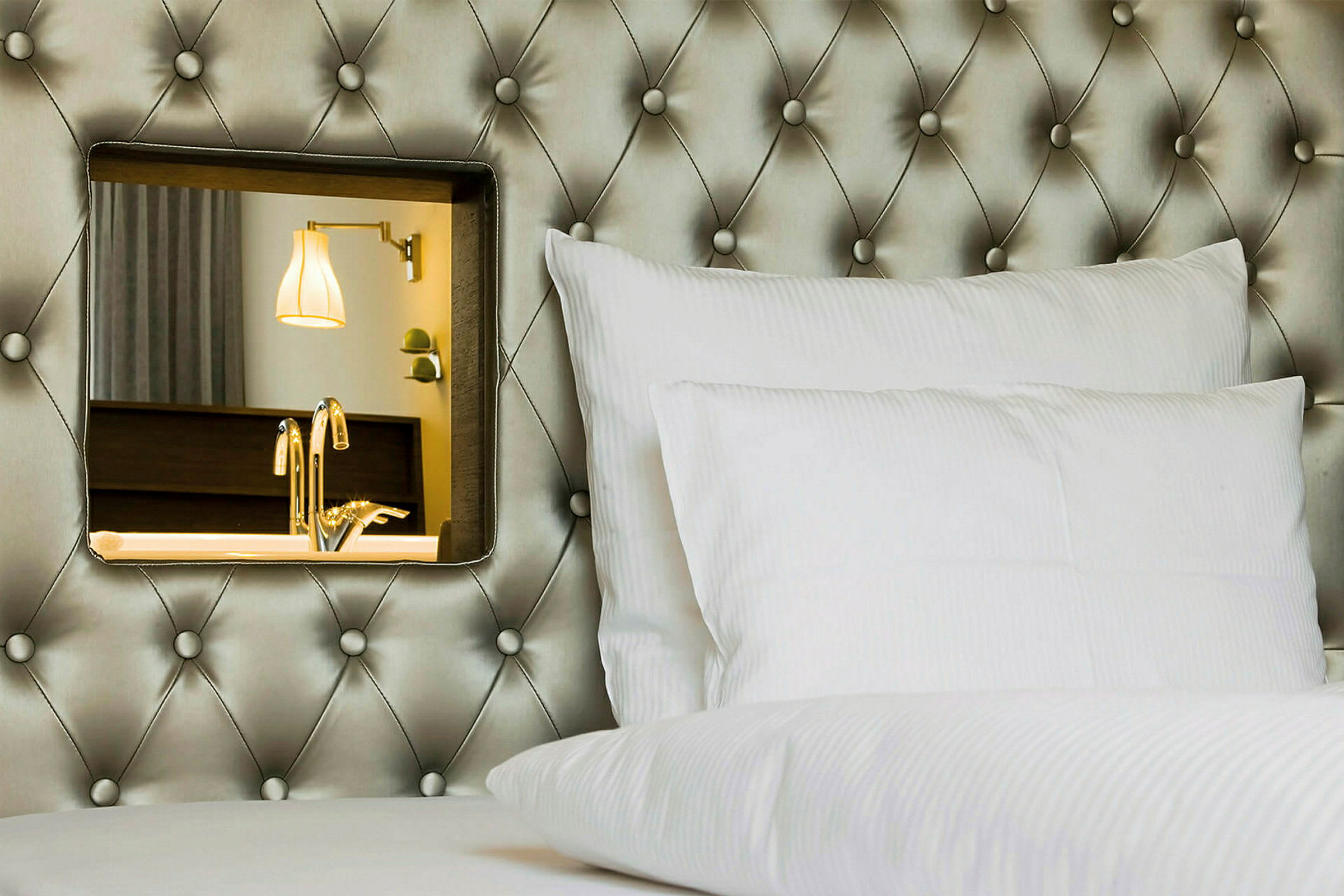 Hotellsäng med vit kudde och dekorativ spegel på den stoppade huvudgaveln. (AI-genererad text)
