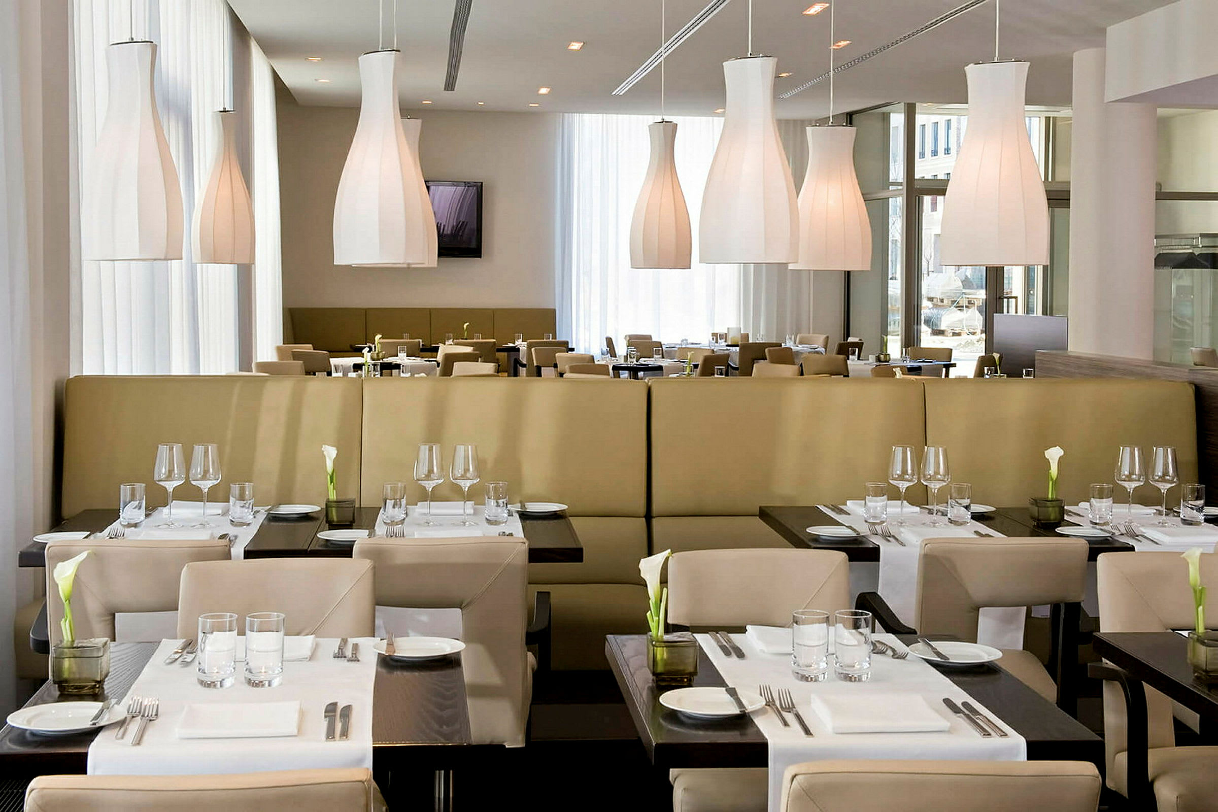 En restaurang med moderna möbler och dukade bord. Ljusa hängande lampor syns i taket. (AI-genererad text)