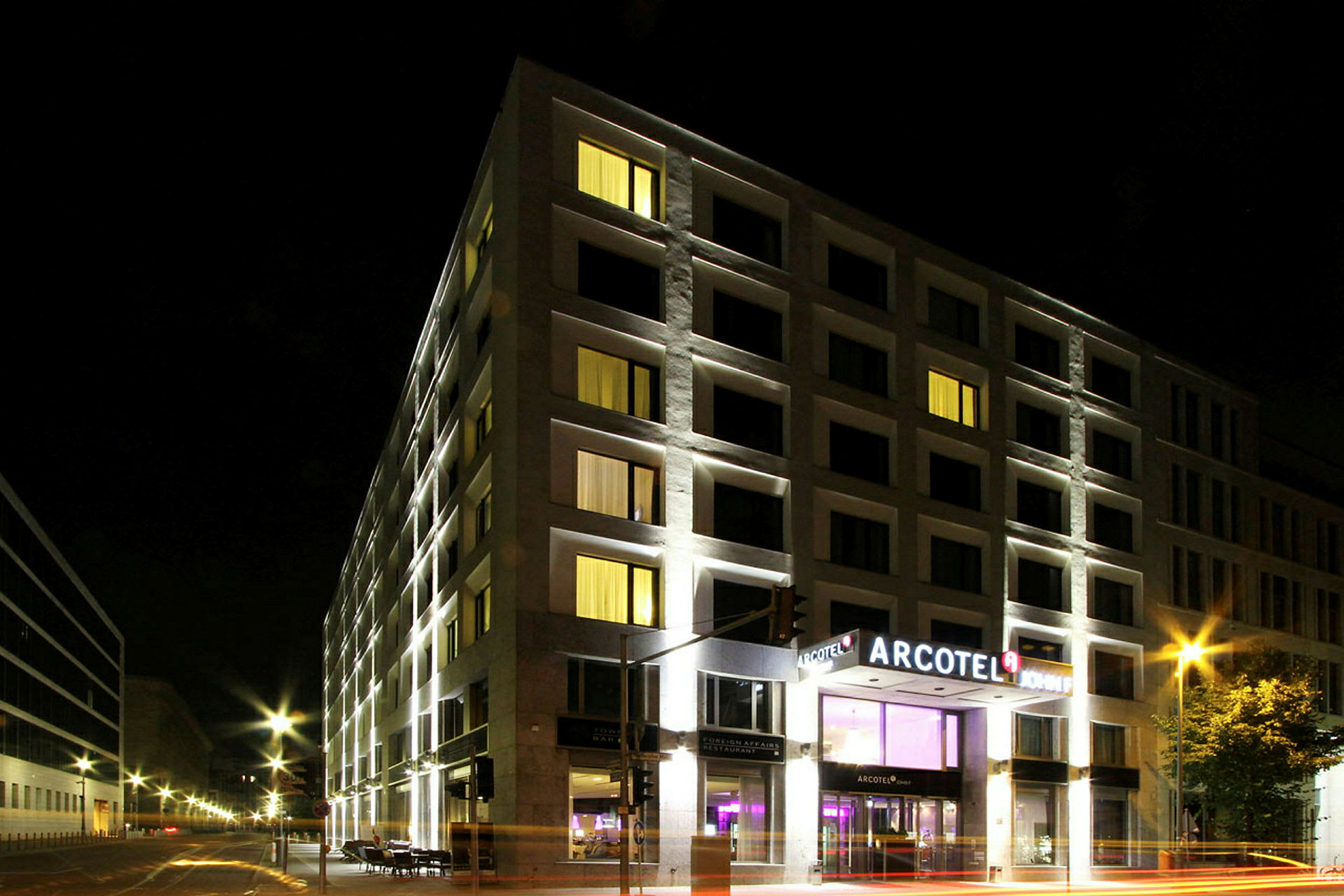 Ett hotell upplyst på kvällen med Arcotel-skylten vid entrén. (AI-genererad text)