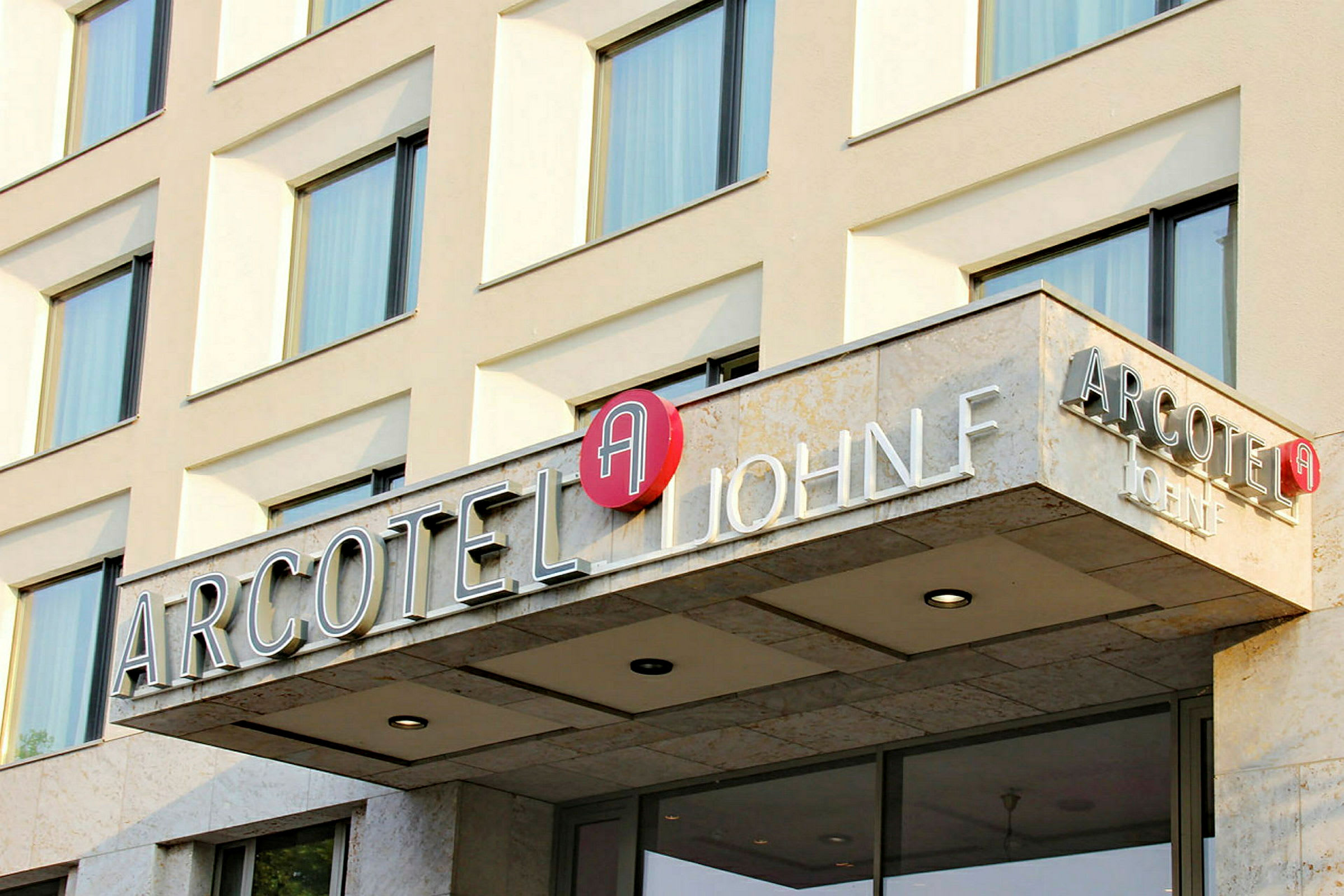 Fasad av hotellbyggnad med skylt som lyder "Arcotel John F". (AI-genererad text)