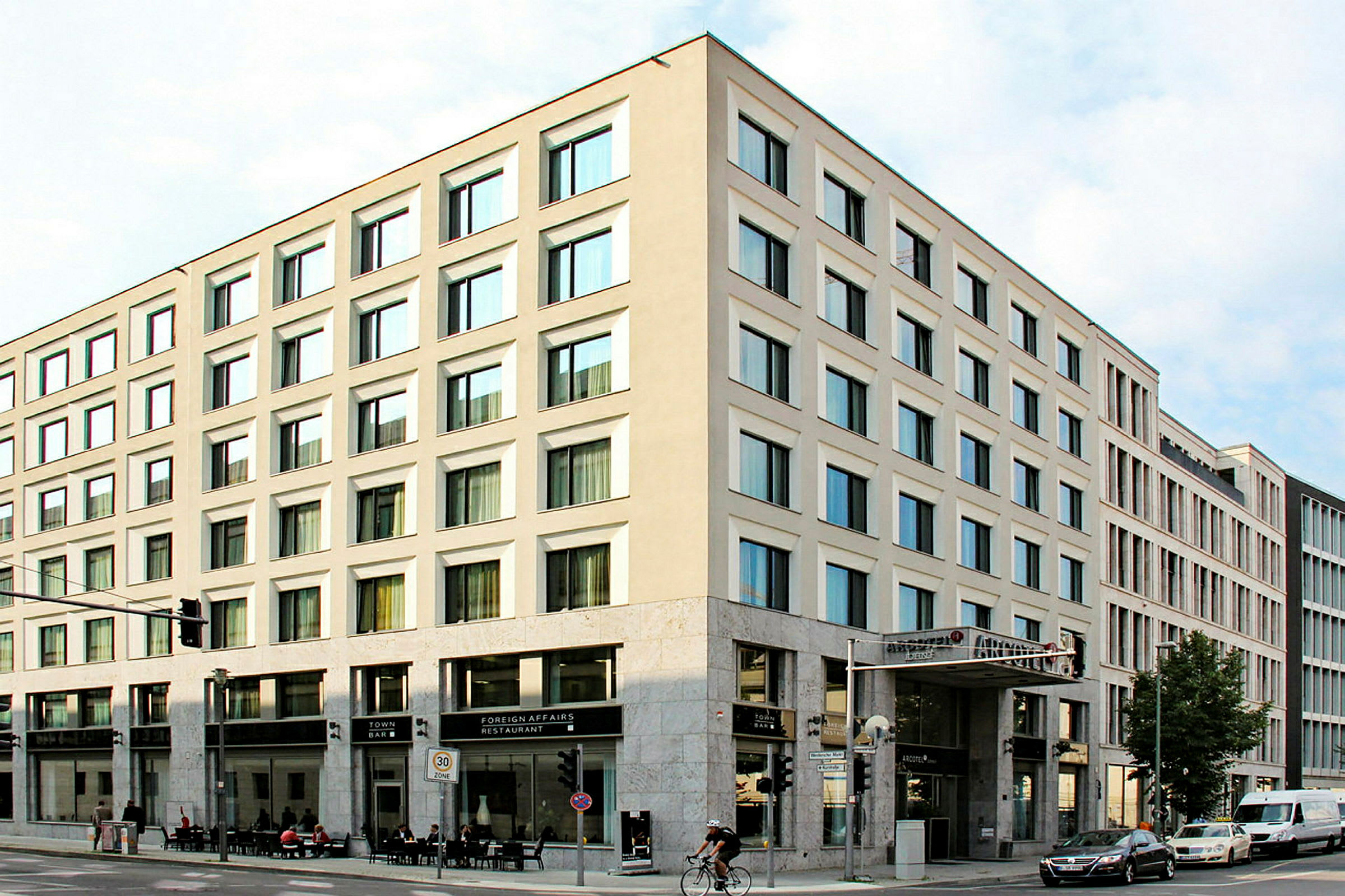 Ett hörnhus med moderna fasader och stora fönster, med restaurang och bar på bottenvåningen. (AI-genererad text)
