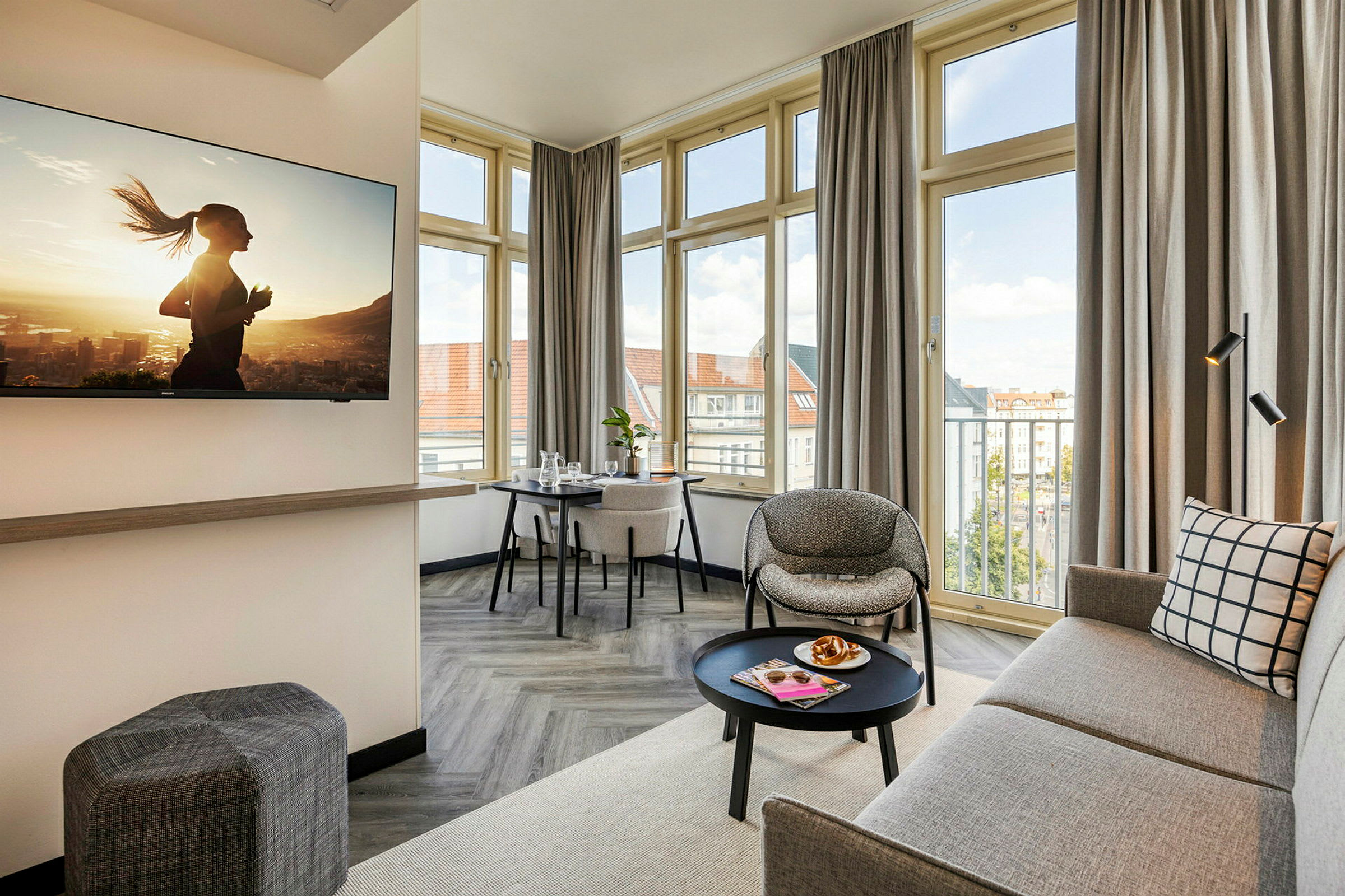 En modern och ljus hotellsvit med soffa, fåtölj, bord och en TV på väggen. (AI-genererad text)