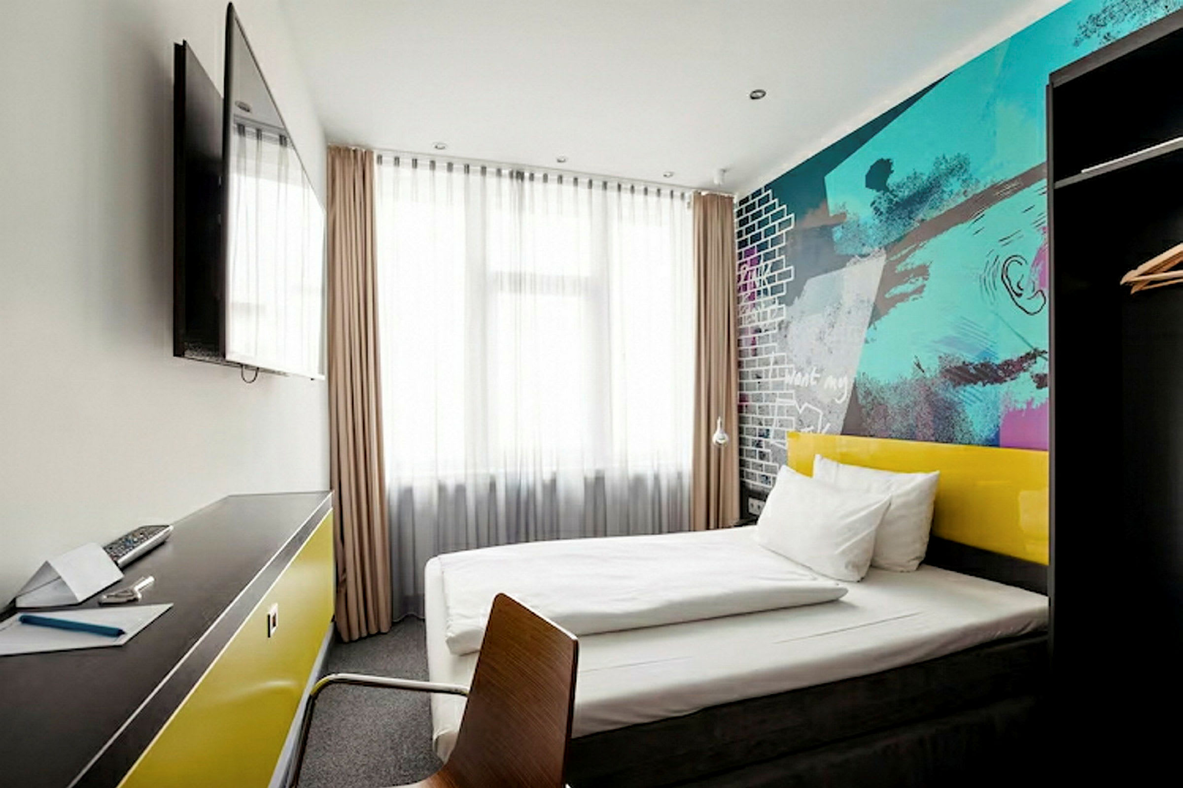 Ett modernt hotellrum med en säng, färgglada väggar och ett skrivbord med en TV på väggen. (AI-genererad text)