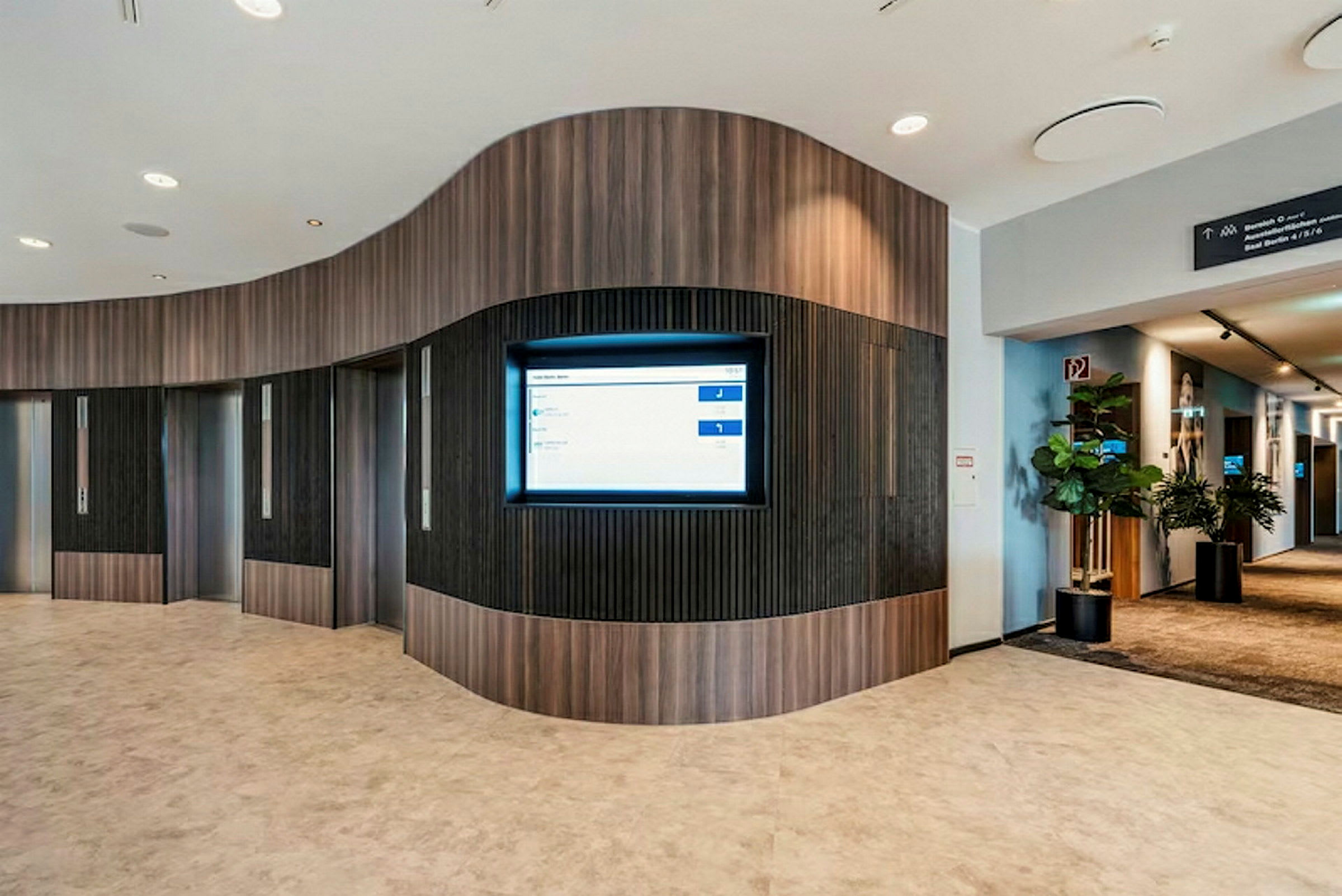 Interiör av en modern lobby med hissar och en informationsskärm på väggen. (AI-genererad text)