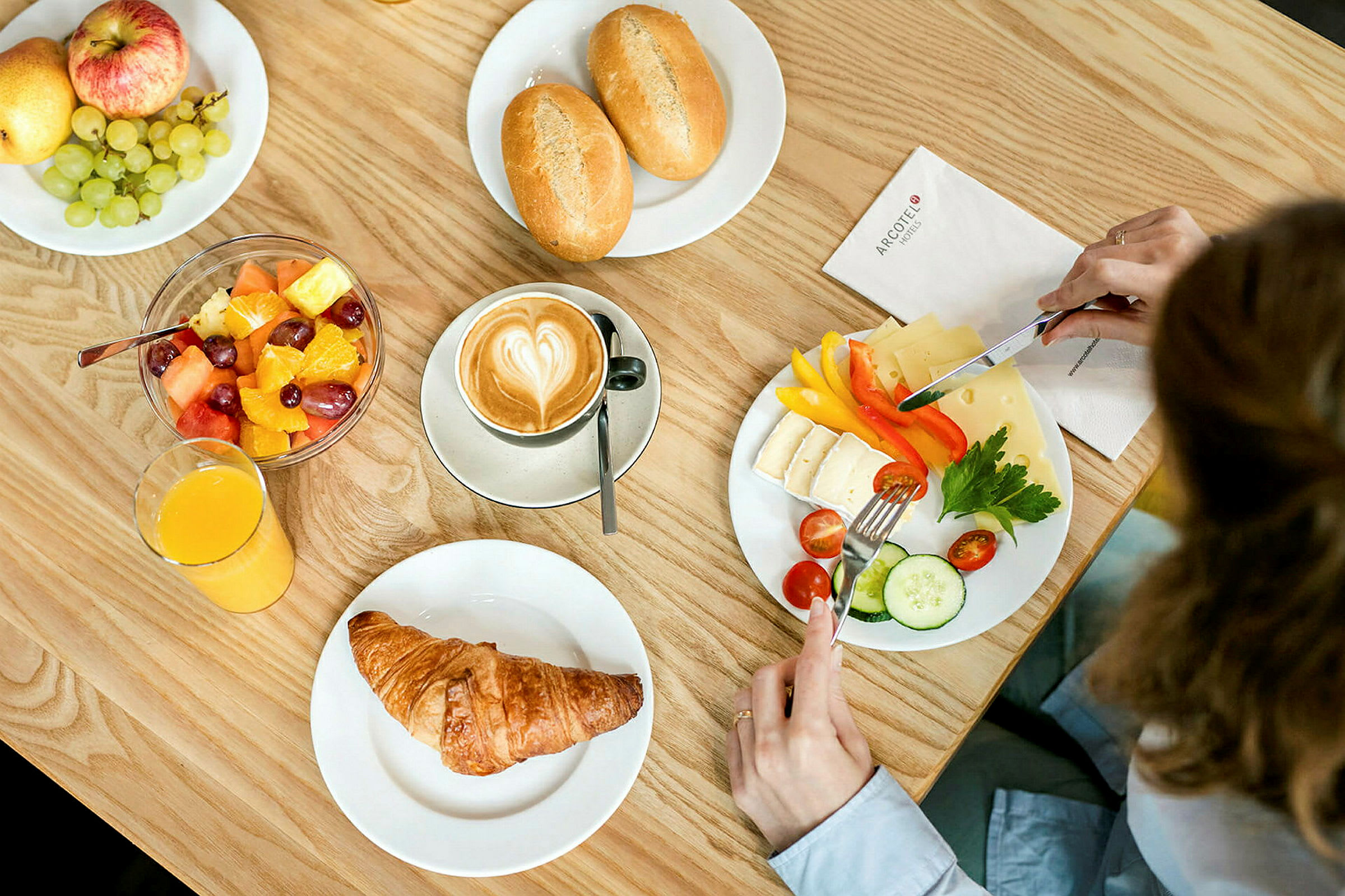 En frukost med kaffe, croissant, fruktsallad, ost, grönsaker och bröd. (AI-genererad text)