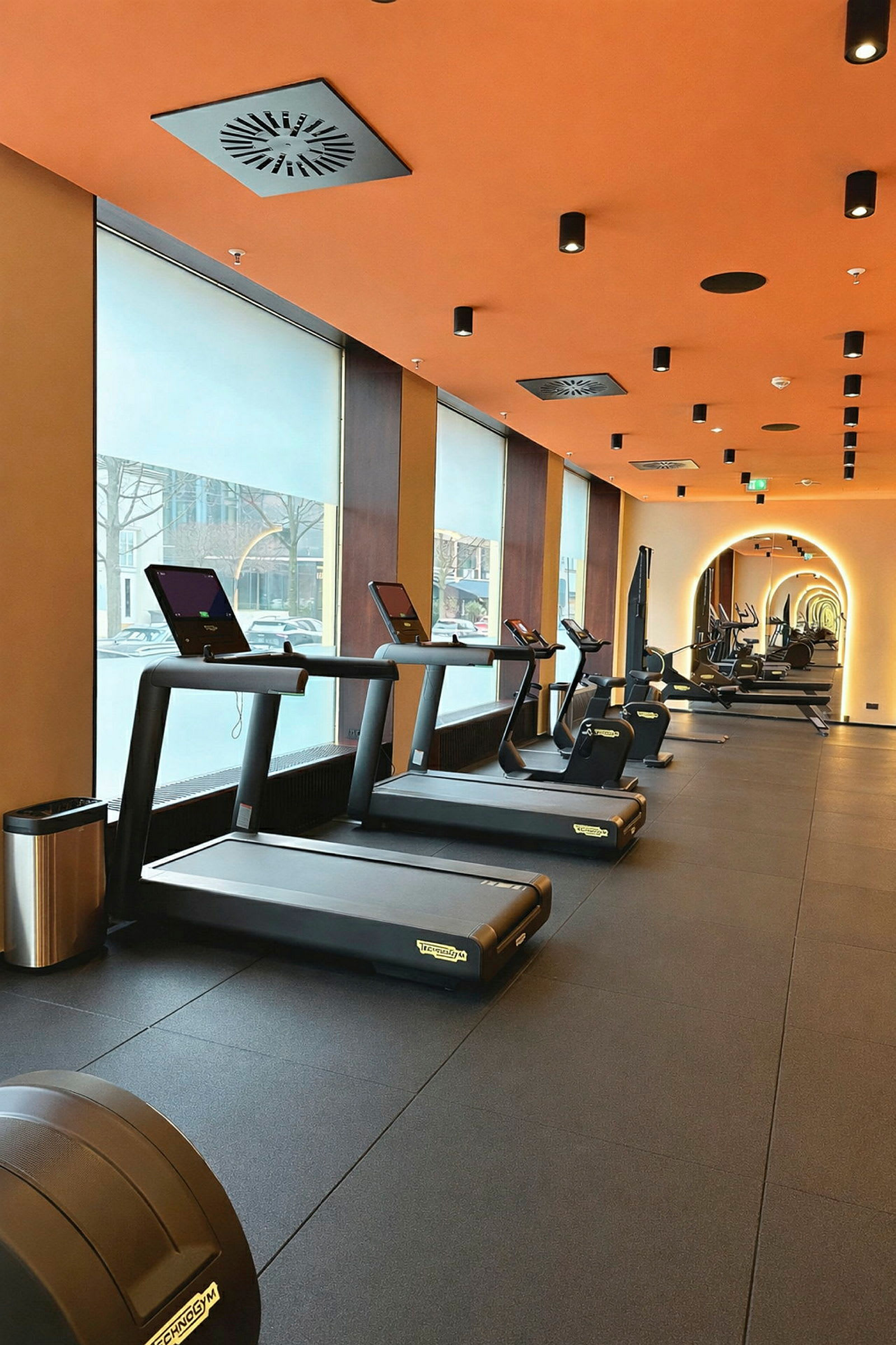 Ett gym med flera löpband som står framför stora fönster. (AI-genererad text)
