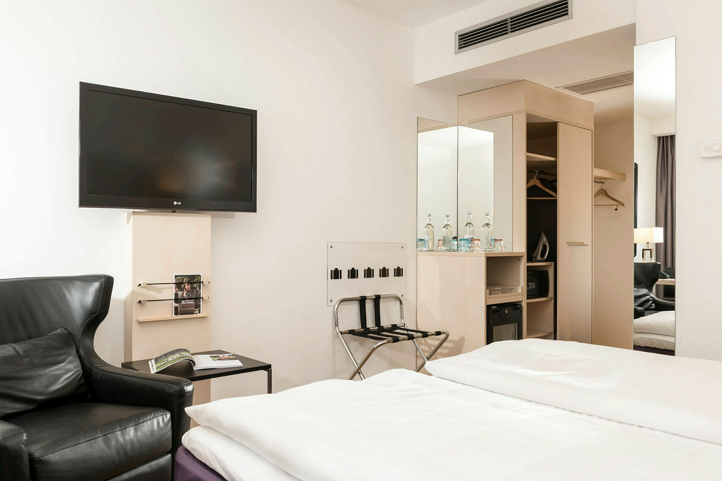 Ett hotellrum med sängar, en svart fåtölj, en väggmonterad TV och garderob. (AI-genererad text)