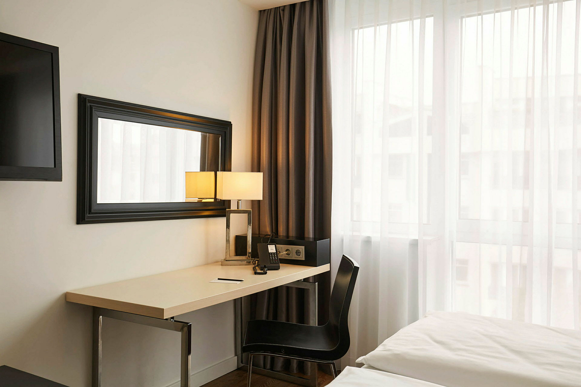 Ett hotellrum med ett skrivbord, spegel, säng och ett fönster. (AI-genererad text)