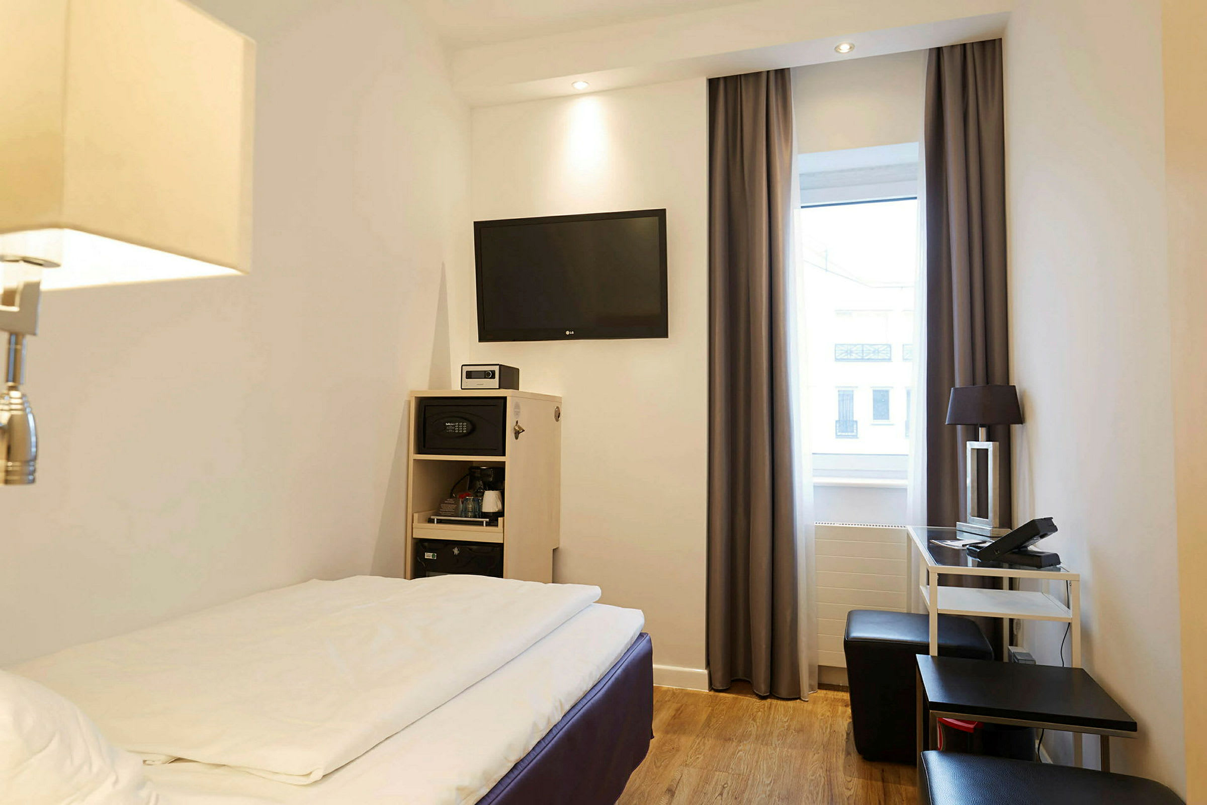 Ett hotellrum med en säng, TV på väggen och möbler såsom ett skrivbord och stol. (AI-genererad text)