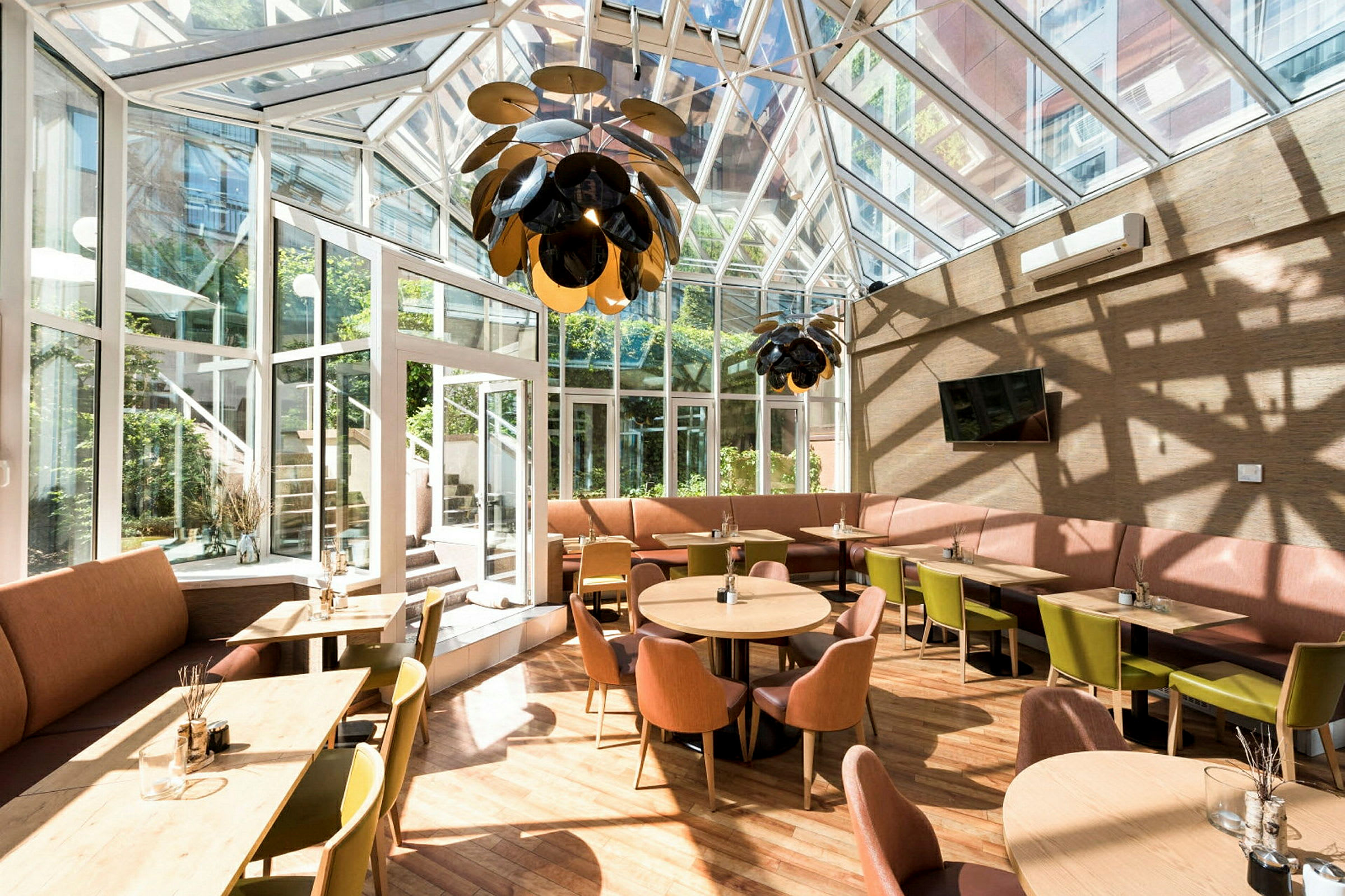 Ett ljust möblerat kafé med stora fönster och tak i glas. (AI-genererad text)