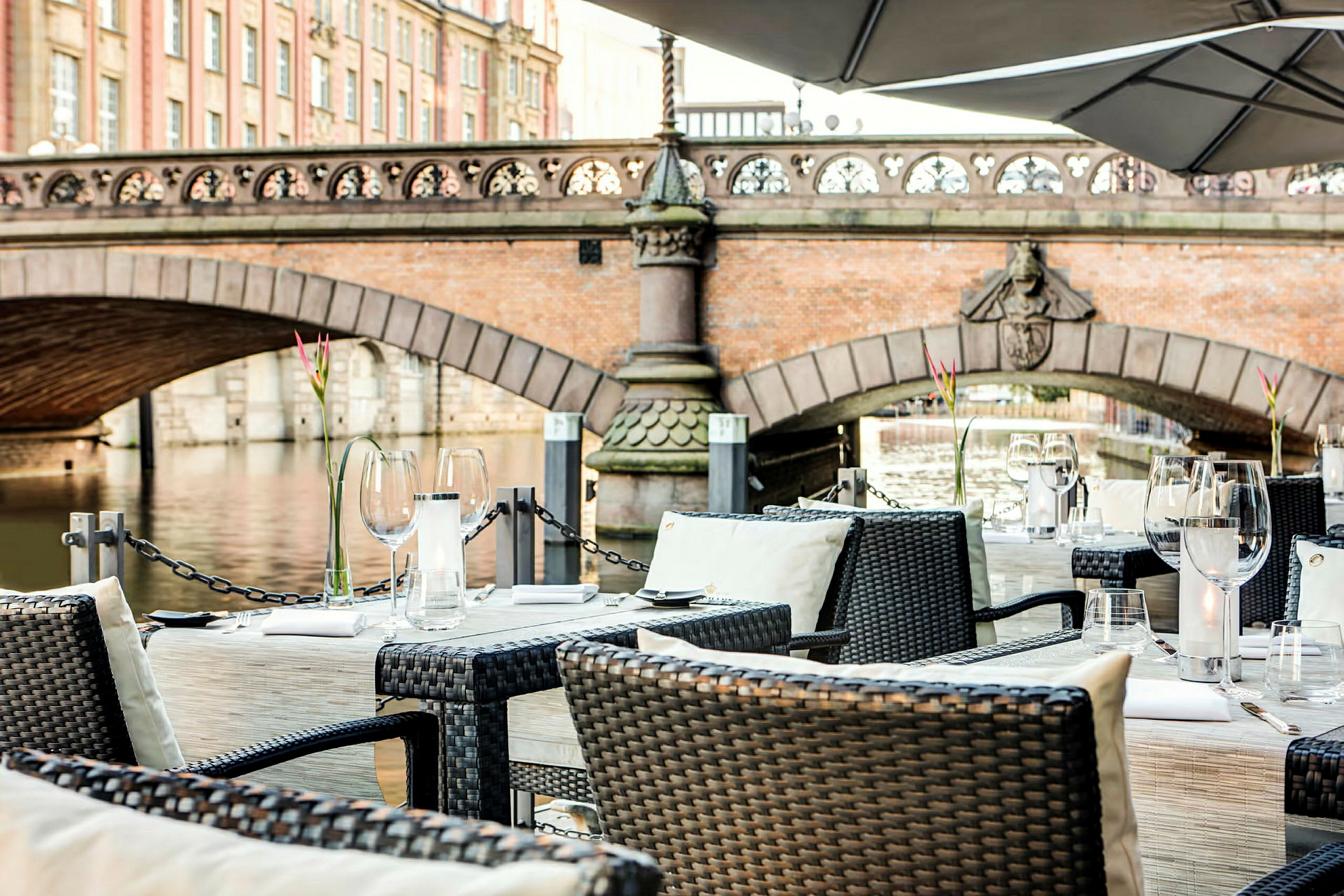 Välkomponerade bordsdukningar på en terrass med utsikt över en bro och en vattendrag. (AI-genererad text)