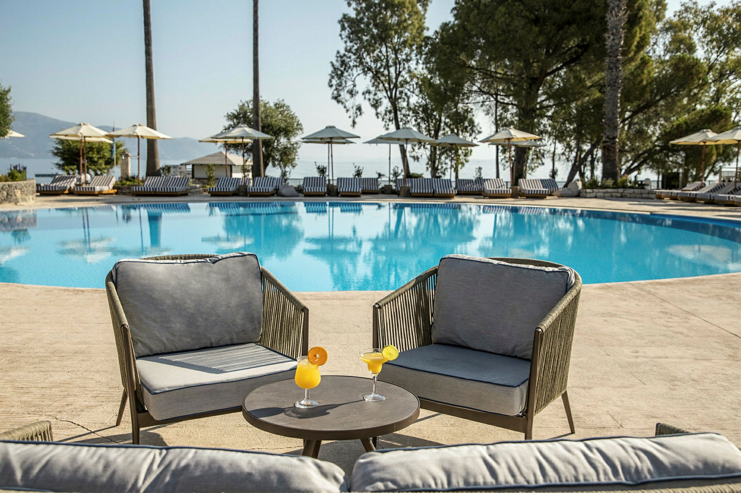 Två fåtöljer med bord och cocktails vid en pool med solstolar i bakgrunden. (AI-genererad text)