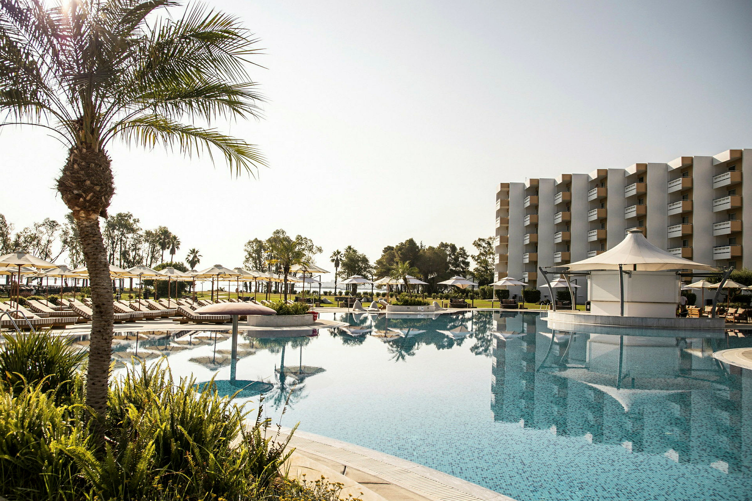 Hotellets poolområde med solstolar, parasoller och en byggnad i bakgrunden. (AI-genererad text)
