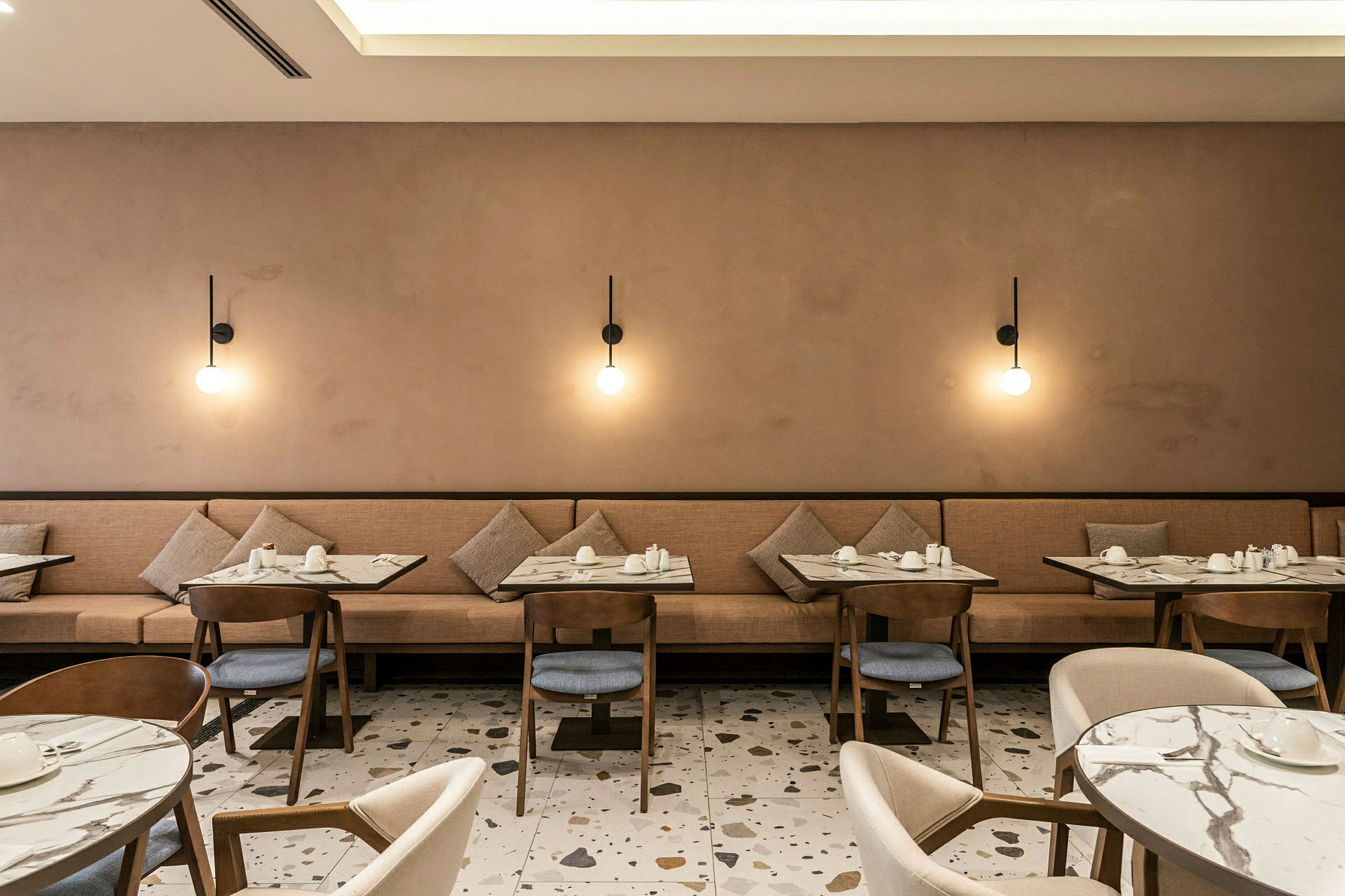 Restaurang med bord och stolar, samt beige soffa och vägglampor. (AI-genererad text)