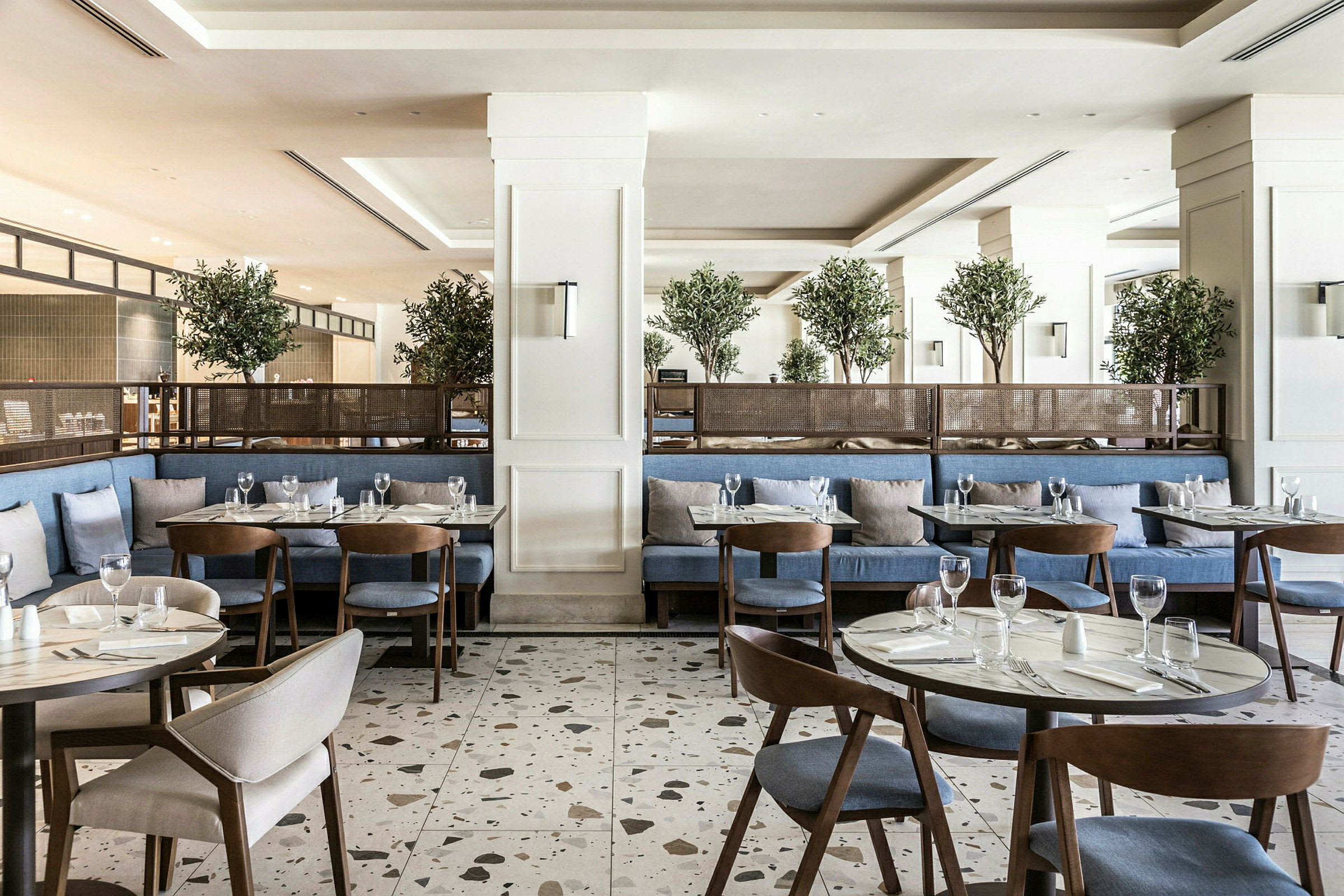 En modern restaurang med blå sittplatser, träbord och gröna växter som dekoration. (AI-genererad text)
