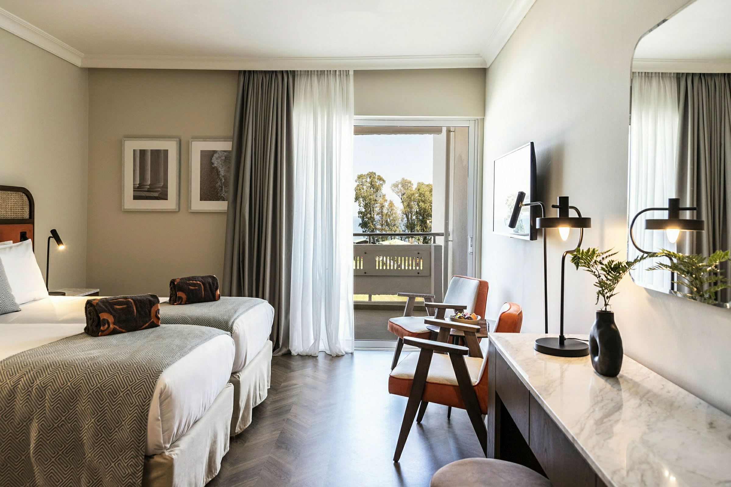 Hotellrum med två enkelsängar, sittgrupp och skrivbord. Balkong med utsikt över träd. (AI-genererad text)